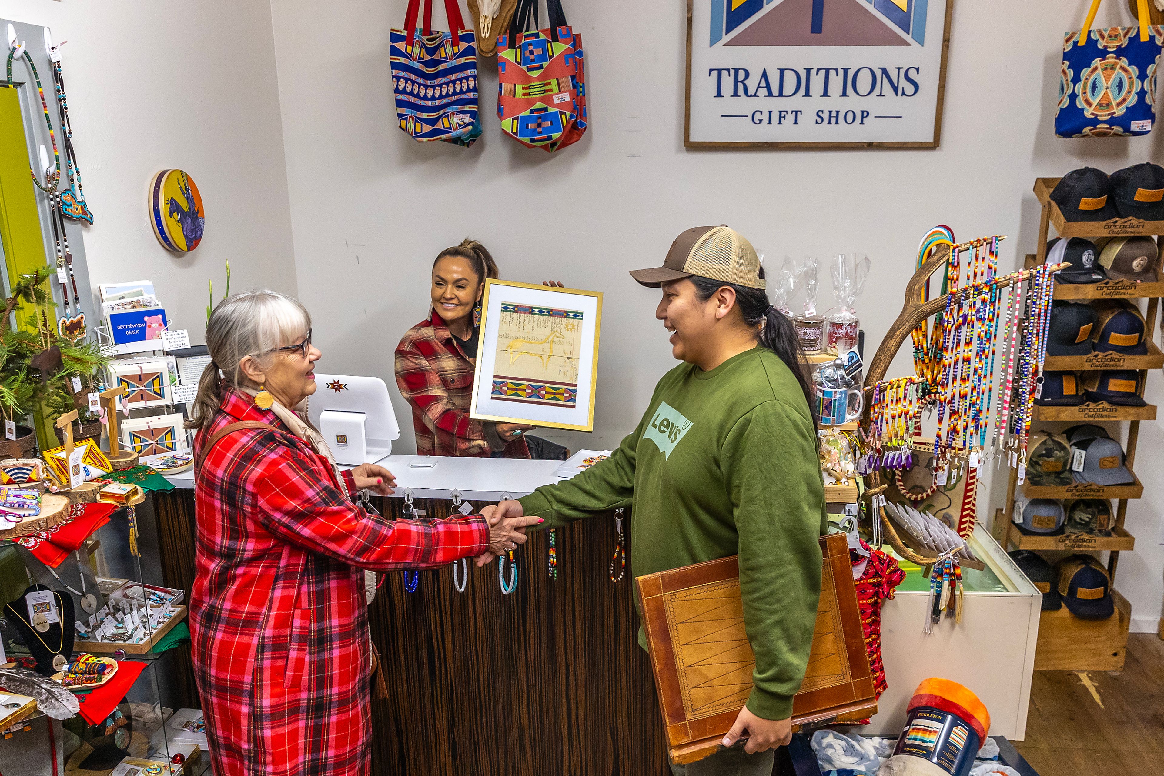 Juli Thorson, of Troy, shakes hands with artist Merlin KW, of Lapwai, after buying an Appaloosa Painting he created on a ledger from 1934, as Stacia Morfin holds the artwork, on Plaid Friday at Nez Perce Traditions Gift Shop. 