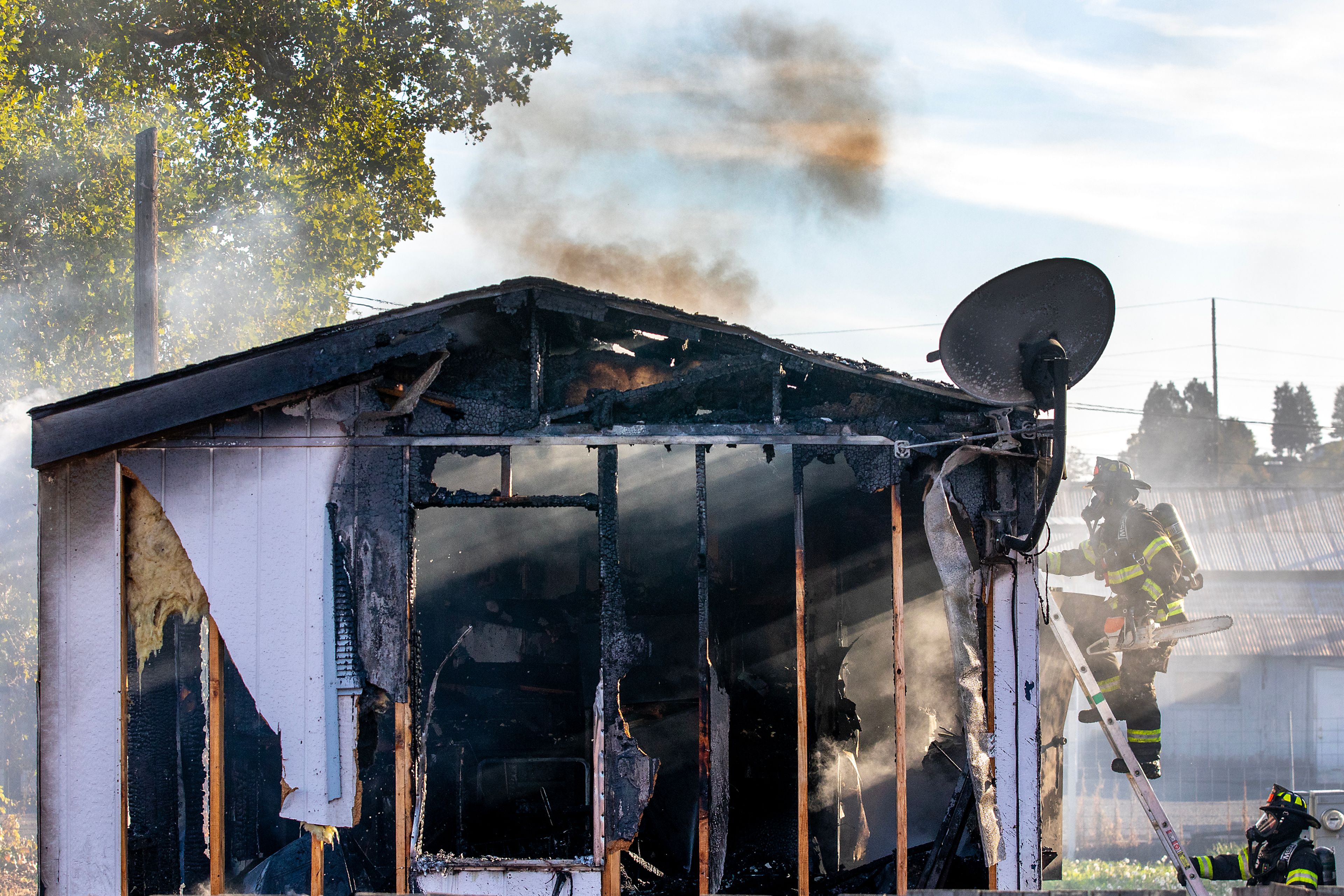 A firefighter climbs up a ladder onto the roof of a smoking mobile home Thursday off 13th Street in Clarkston.