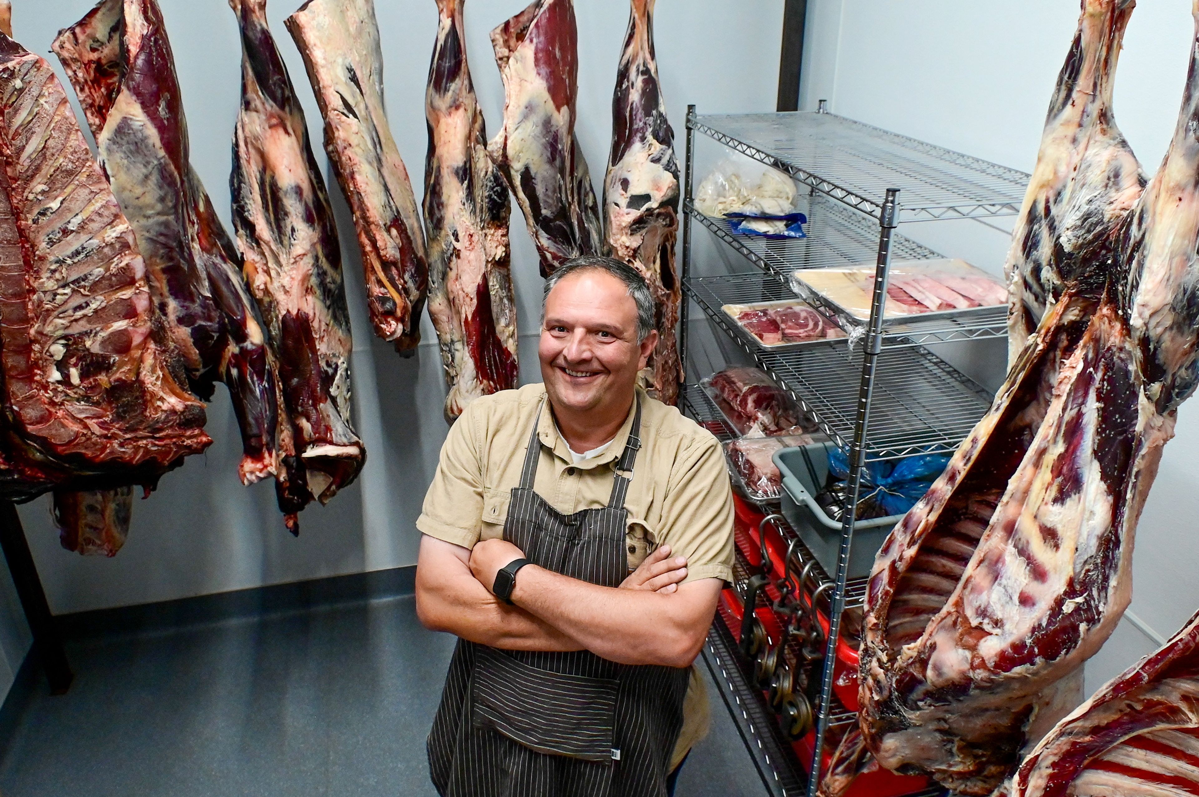 Cow carcasses hang around Gary Moore in a walk-in cooler of The Butcher Shop on Friday in Deary.