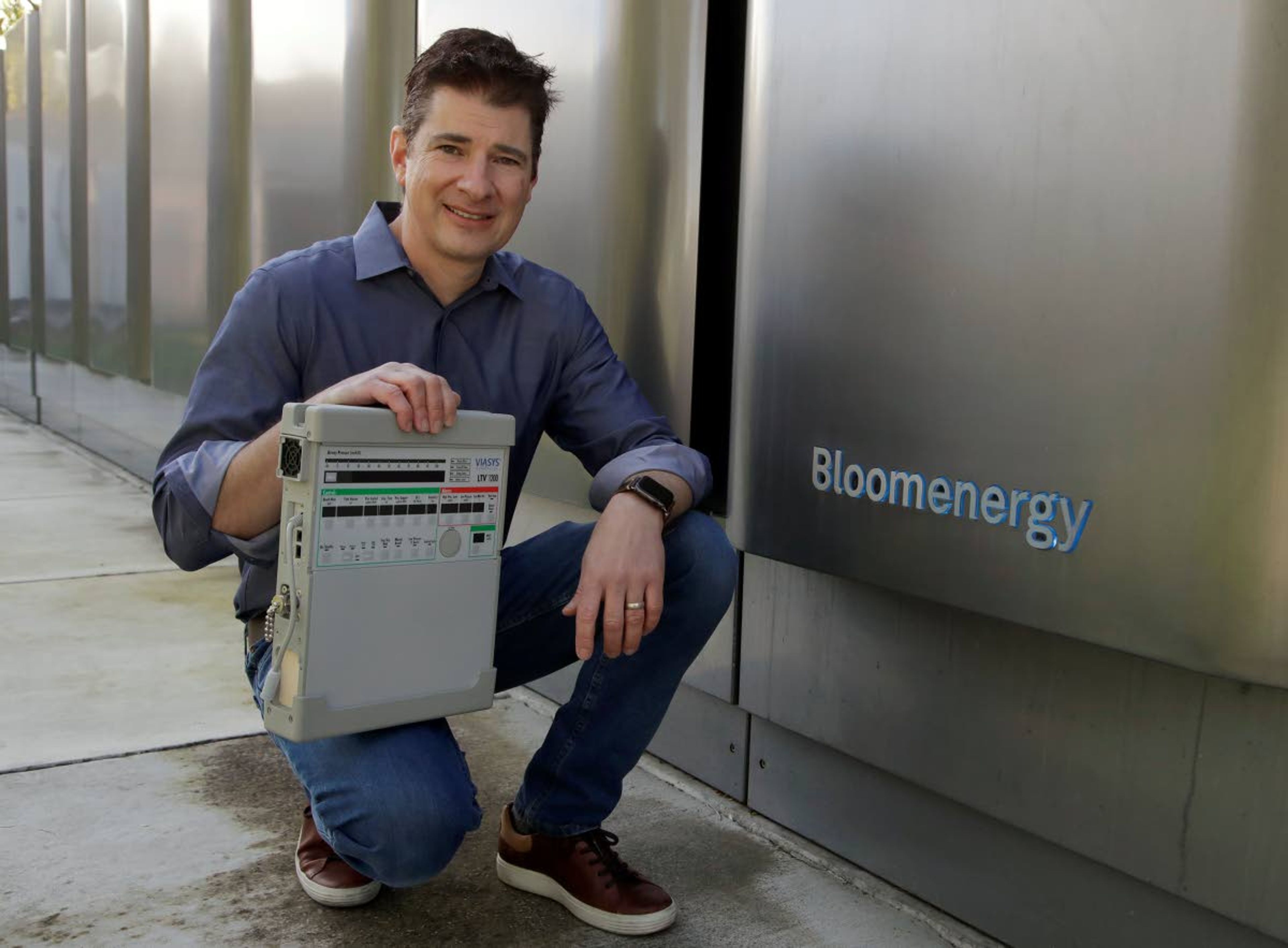 ABOVE: Joe Tavi, Bloom Energy senior director of manufacturing, holds a refurbished ventilator as he kneels beside fuel cells Wednesday in Sunnyvale.