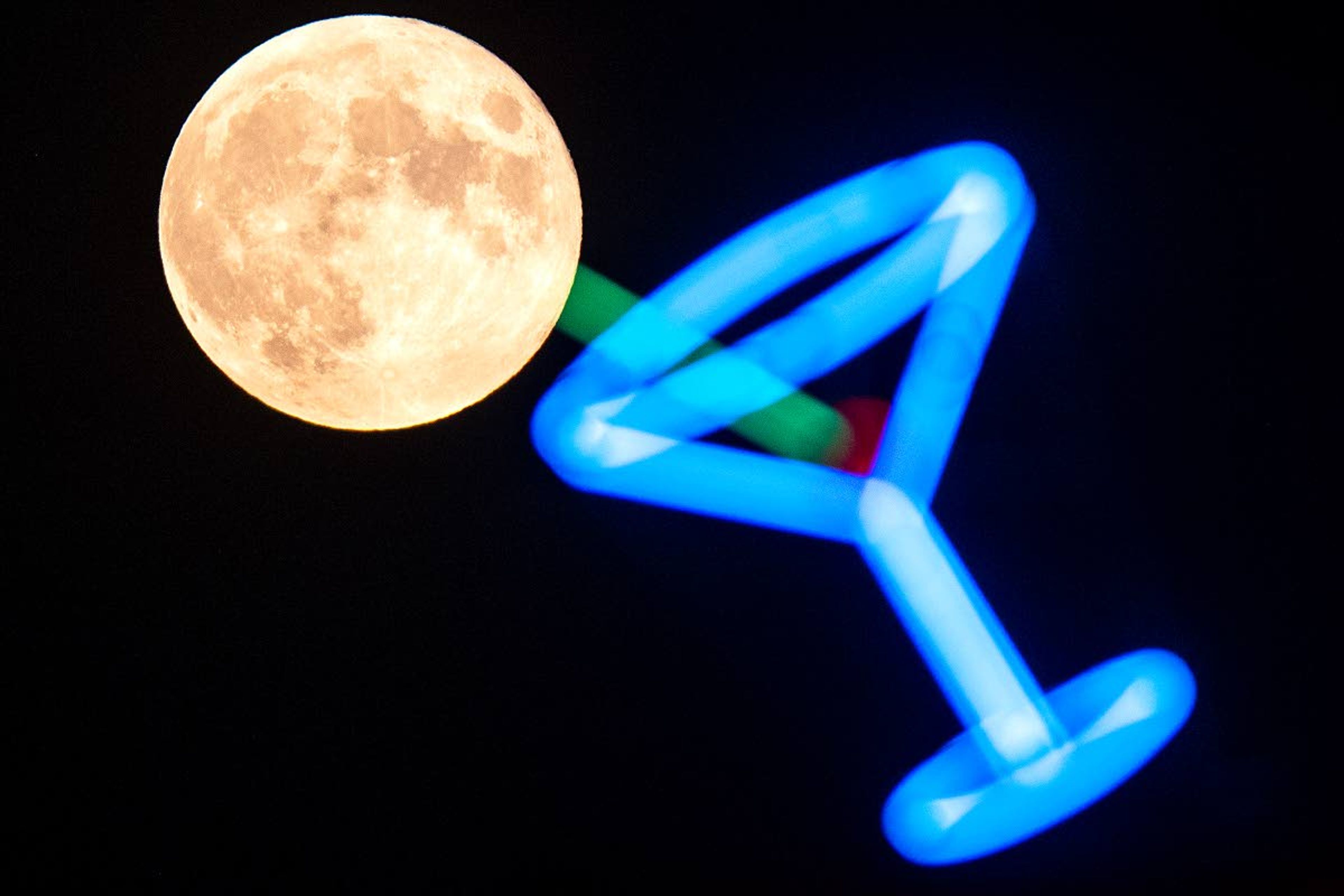 A full moon rises south over the Lewiston Orchards and seemingly greets the tip of a neon martini glass sign above Canter’s Inn along Thain Road on Tuesday night.