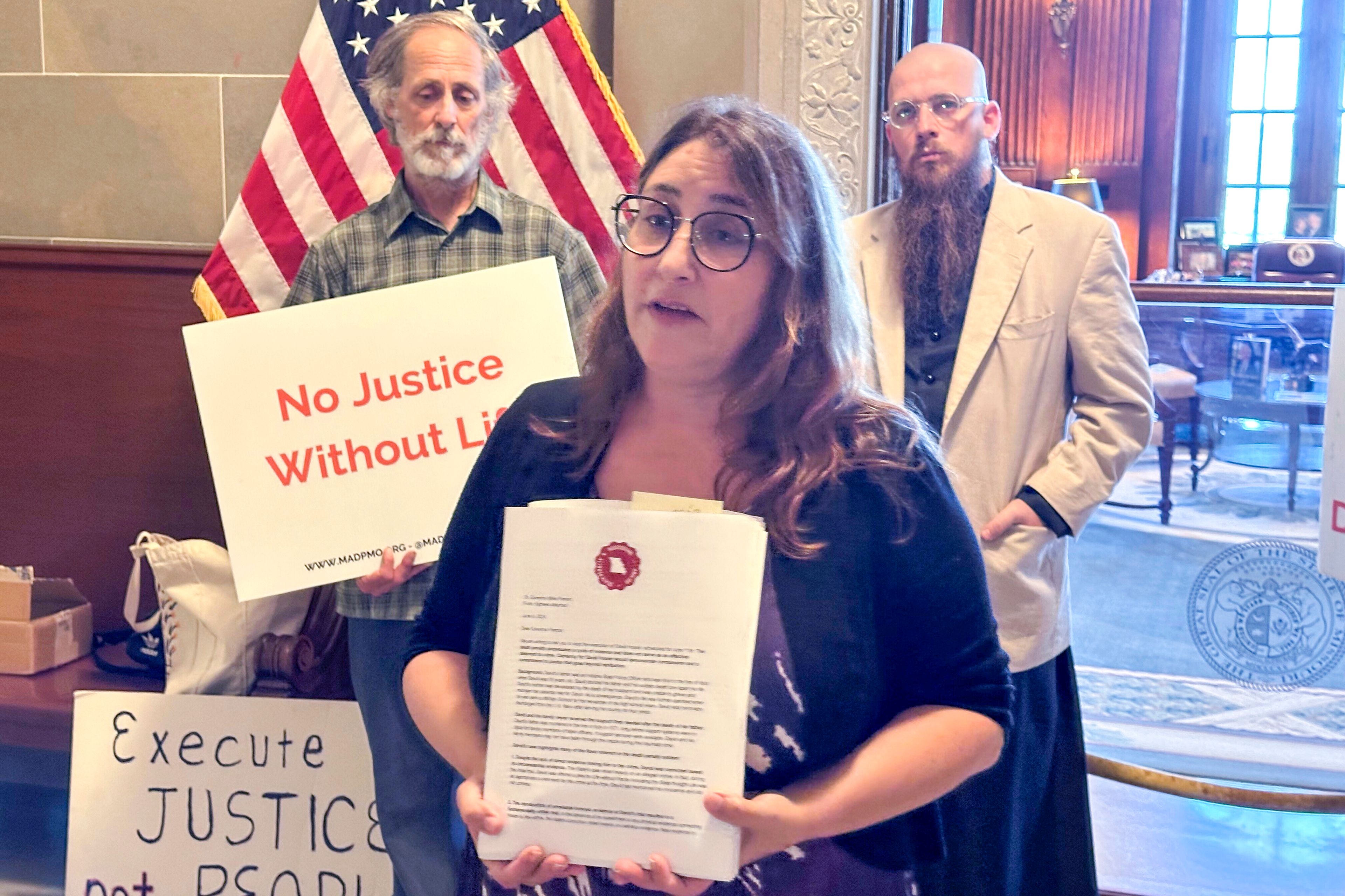 Elyse Max, co-director of Missourians to Abolish the Death Penalty, displays petitions asking Missouri Gov. Mike Parson to grant clemency to death row inmate David Hosier on Thursday, June 6, 2024, outside the governor’s office in the state Capitol, Jefferson City, Missouri. Behind Max, to the right, is the Rev. Jeff Hood, spiritual advisor for inmate David Hosier. The person to the left is not identified.