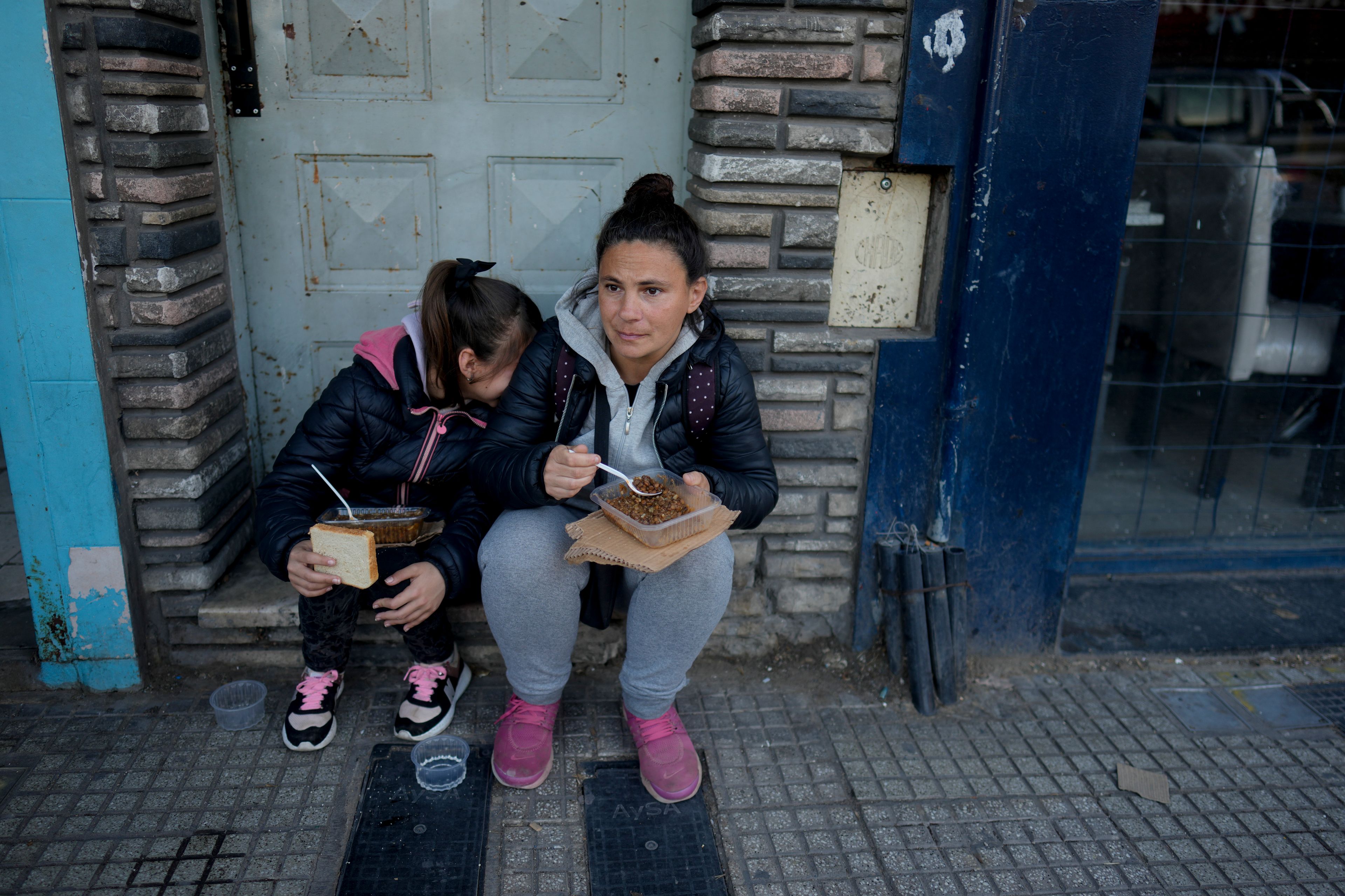 Street vendor Miriam Sidimarco and her daughter Tiziana sit on a door's stoop, to eat a free, cooked meal near the soup kitchen where they received it on the outskirts of Buenos Aires, Argentina, Friday, Sept. 6, 2024. (AP Photo/Natacha Pisarenko)