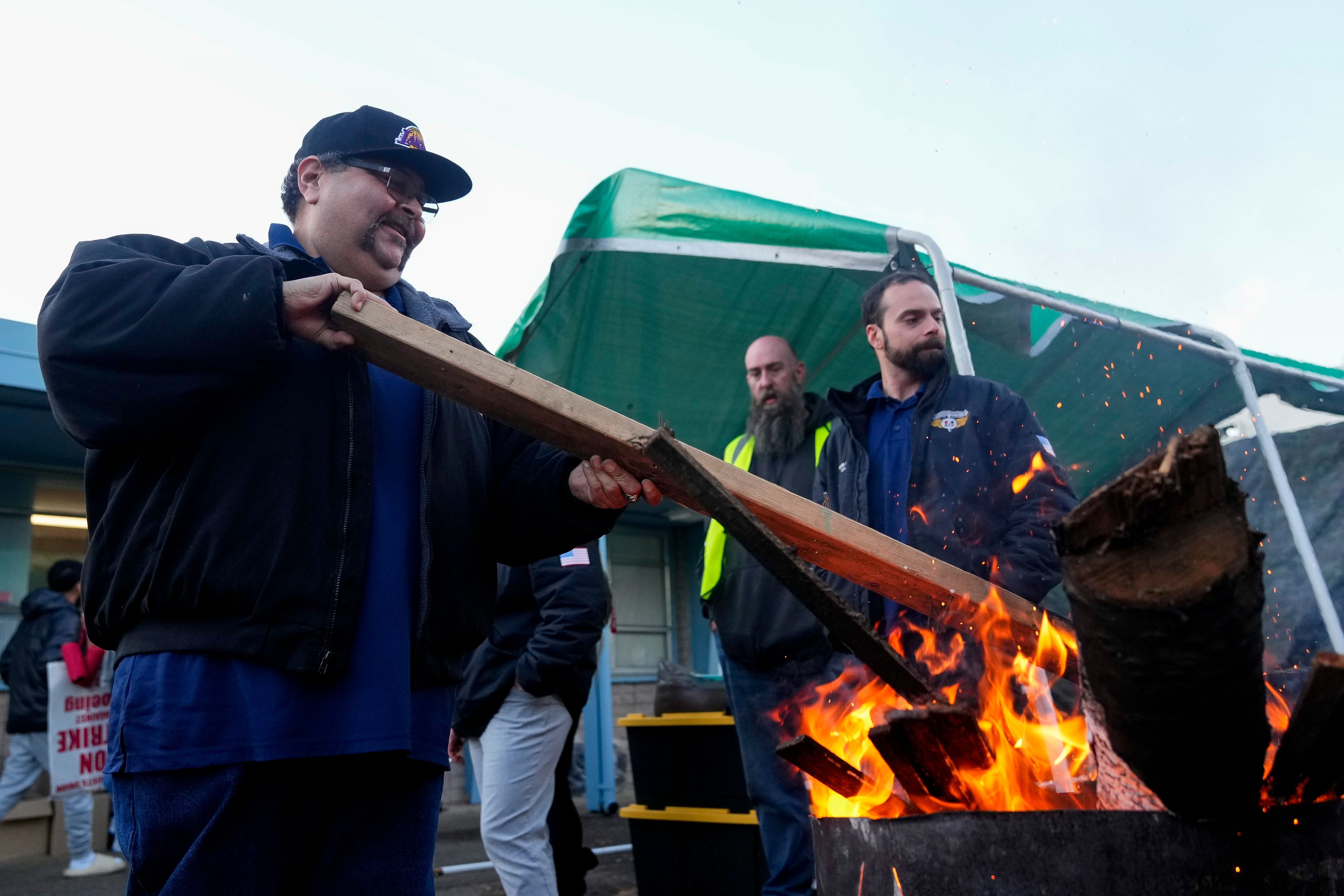 Boeing employee Adrian Camez, who works in Seattle, stokes the fire of a burn barrel as others arrive to vote on a new contract offer from the company Monday, Nov. 4, 2024, at the Aerospace Machinists Union hall in Renton, Wash. (AP Photo/Lindsey Wasson)