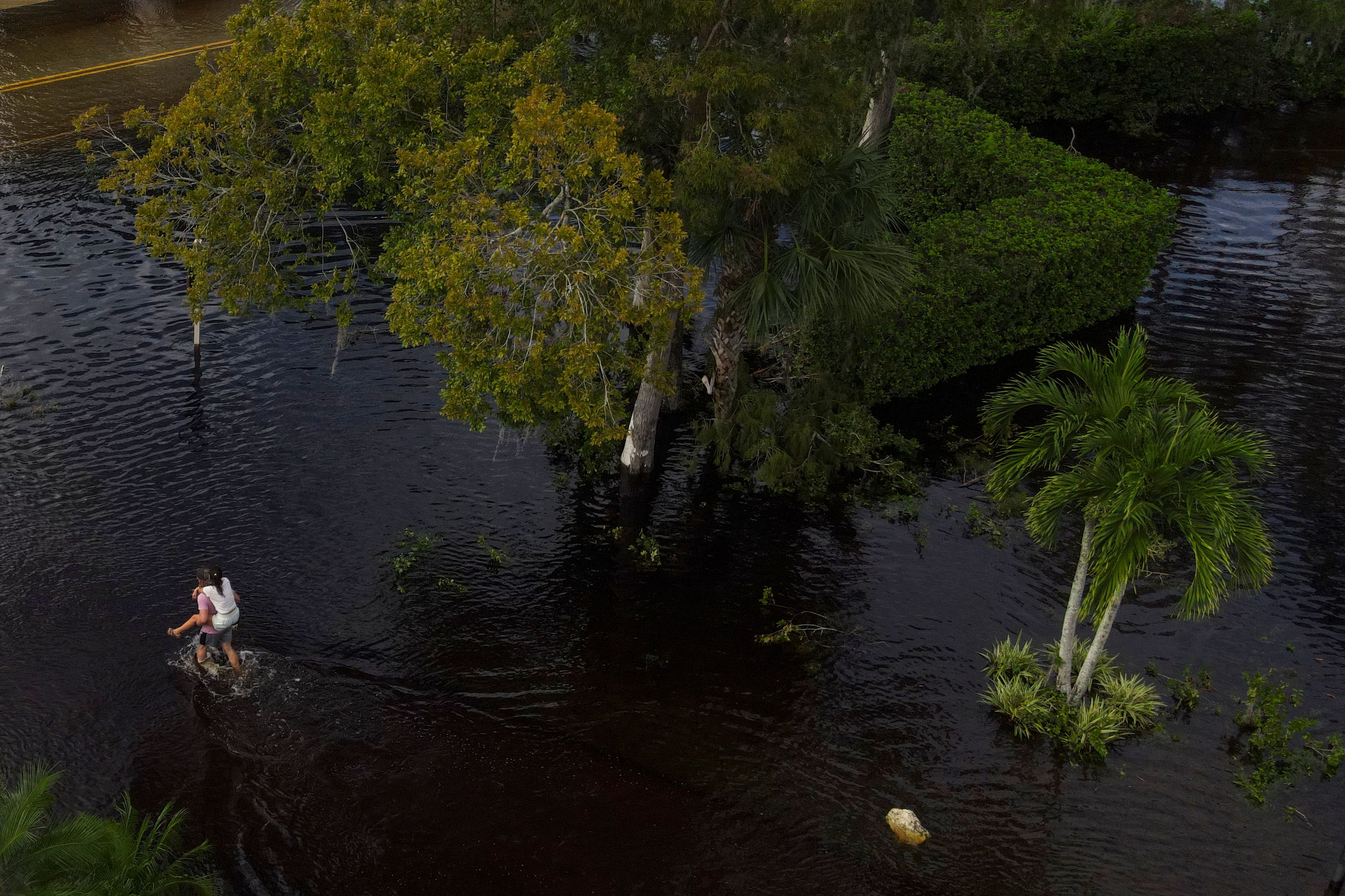 A man carries a woman on his back as they wade through floodwaters in the Tarpon Woods neighborhood of Palm Harbor, Fla., following Hurricane Milton, Friday, Oct. 11, 2024. (AP Photo/Julio Cortez)