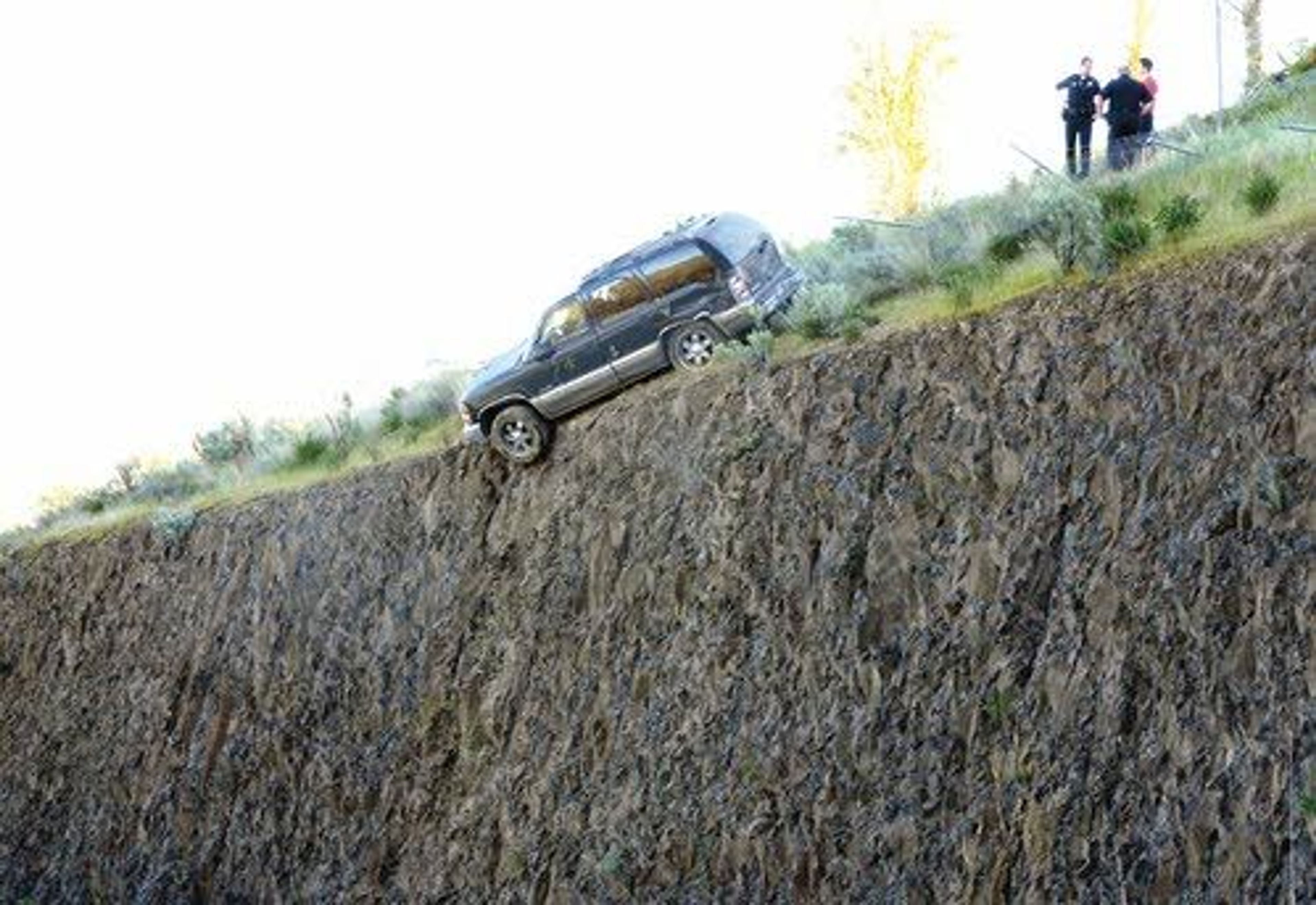 Lewiston police officers talk to the driver of the SUV hanging precariously on the edge of a 20-foot drop onto Bryden Canyon Road, where it was stopped Wednesday morning by a chain-link fence.