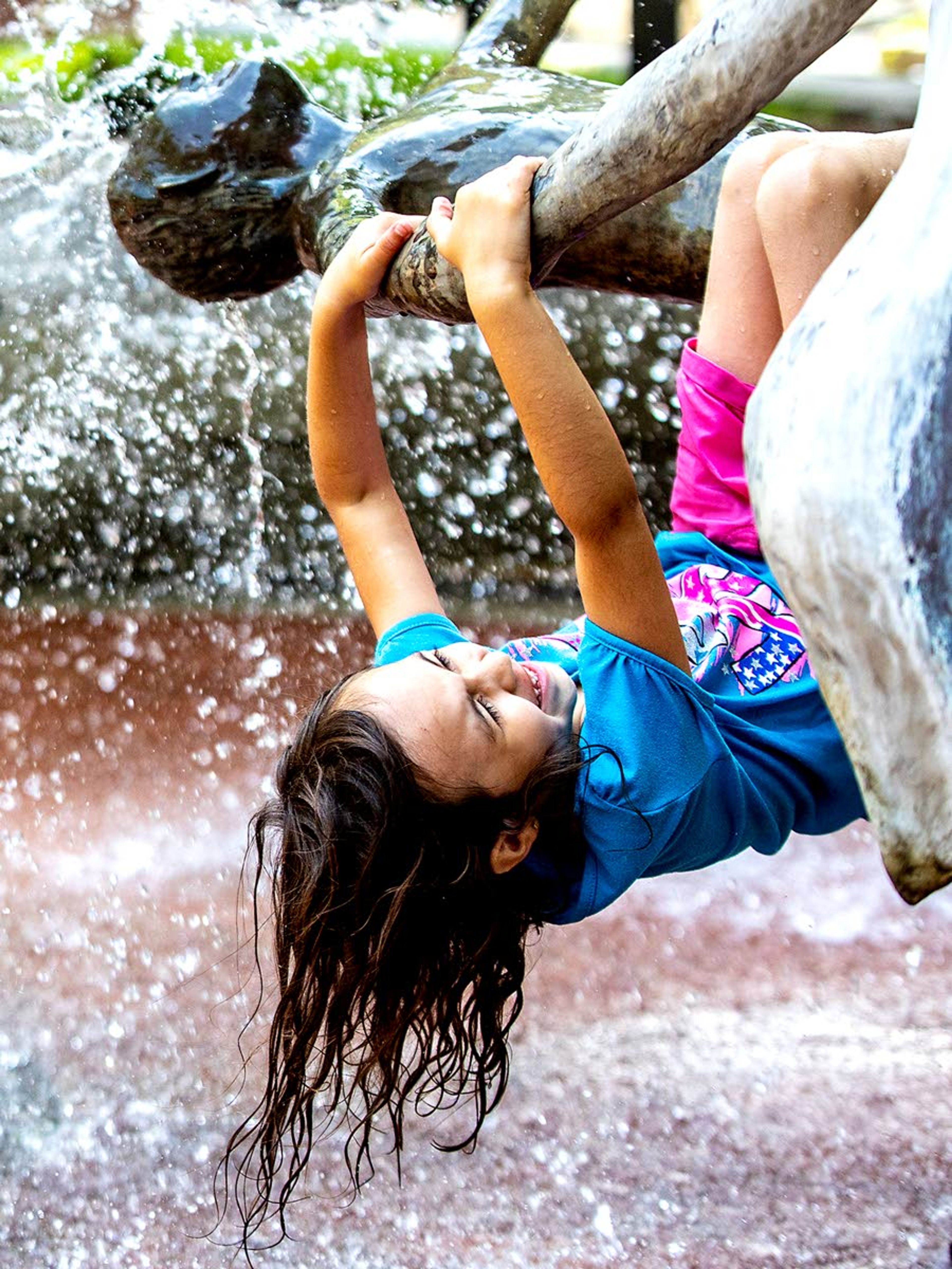 A girl hangs from the arms of the statue at the Brackenbury Square fountain Tuesday in downtown Lewiston. Officials are issuing warnings about the extreme heat as the mercury climbs this week, saying it will increase the potential for heat-related illnesses, especially for those working or participating in outdoor activities.