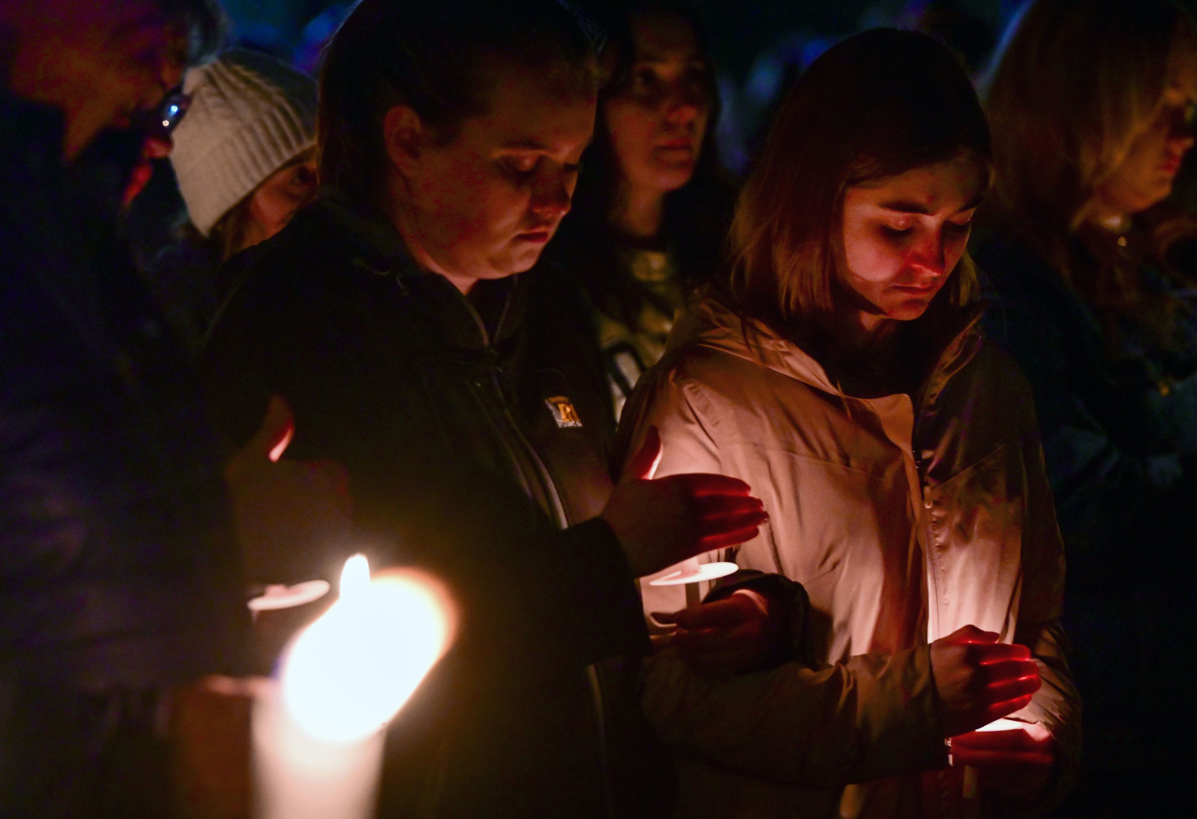 Those gathered for a vigil in honor of the four University of Idaho students killed a year ago look down at their candles as they hear four student speak in memory of those lost—Ethan Chapin, Xana Kernodle, Madison Mogen and Kaylee Goncalves.