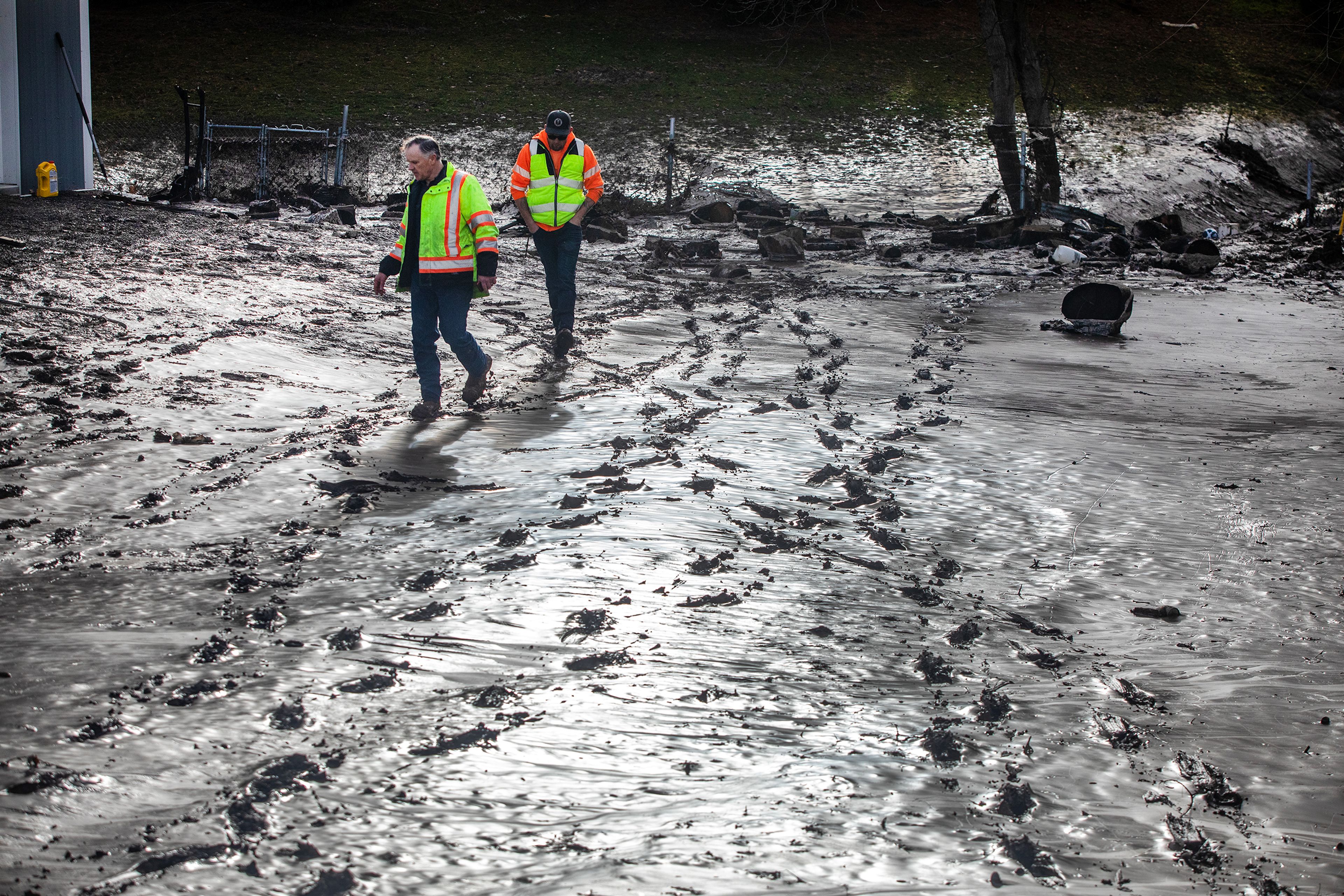 City workers walk through a yard that has been covered in mud from the water reservoir burst, off of Sunset Drive Wednesday in Lewiston.