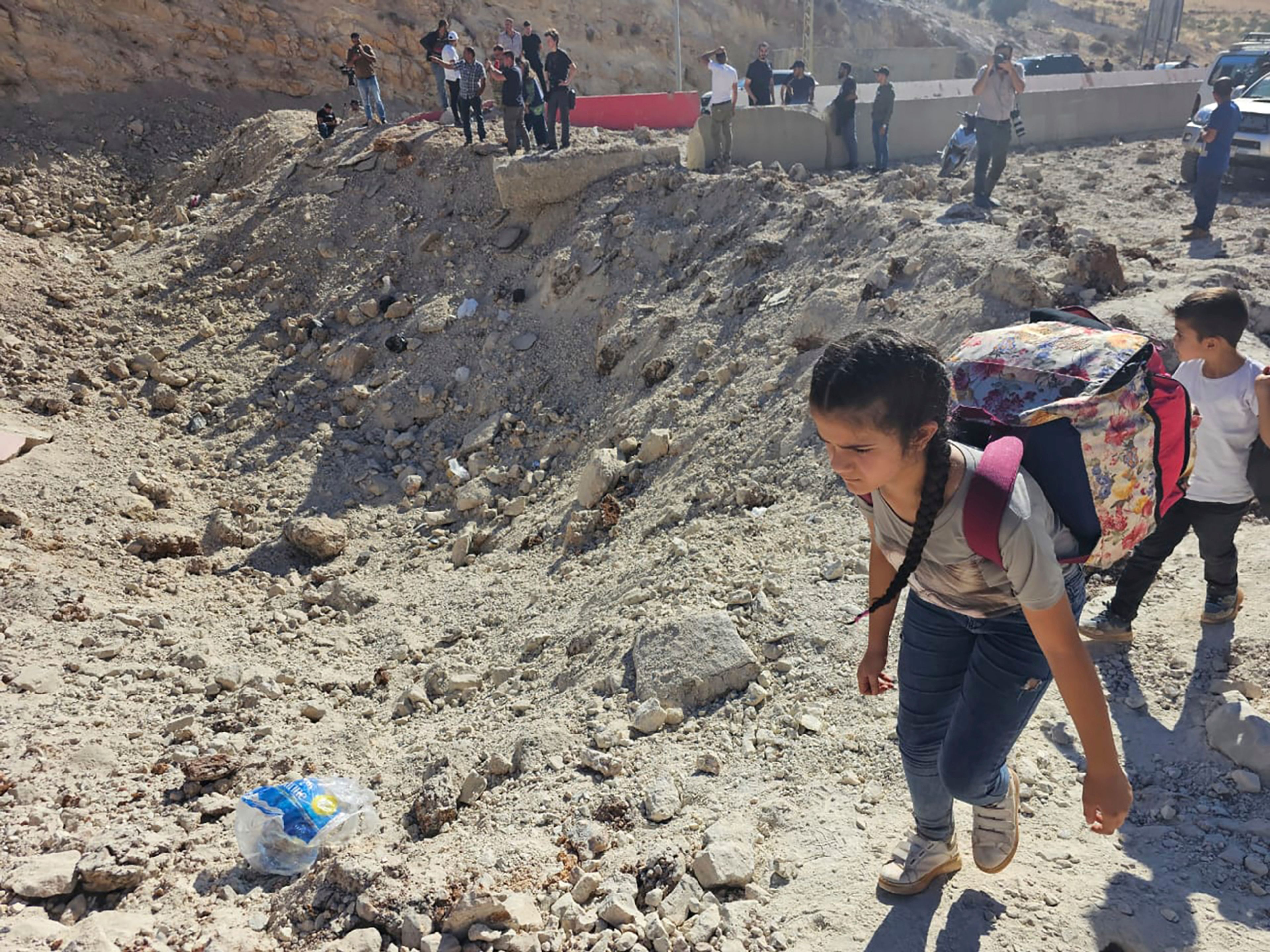 A girl carries her belongings crossing on foot into Syria through a crater caused by an Israeli airstrike to cut the road between the Lebanese and the Syrian checkpoints, at the Masnaa crossing, in the eastern Bekaa Valley, Lebanon, Friday, Oct. 4, 2024. (AP Photo/Samer Husseini)