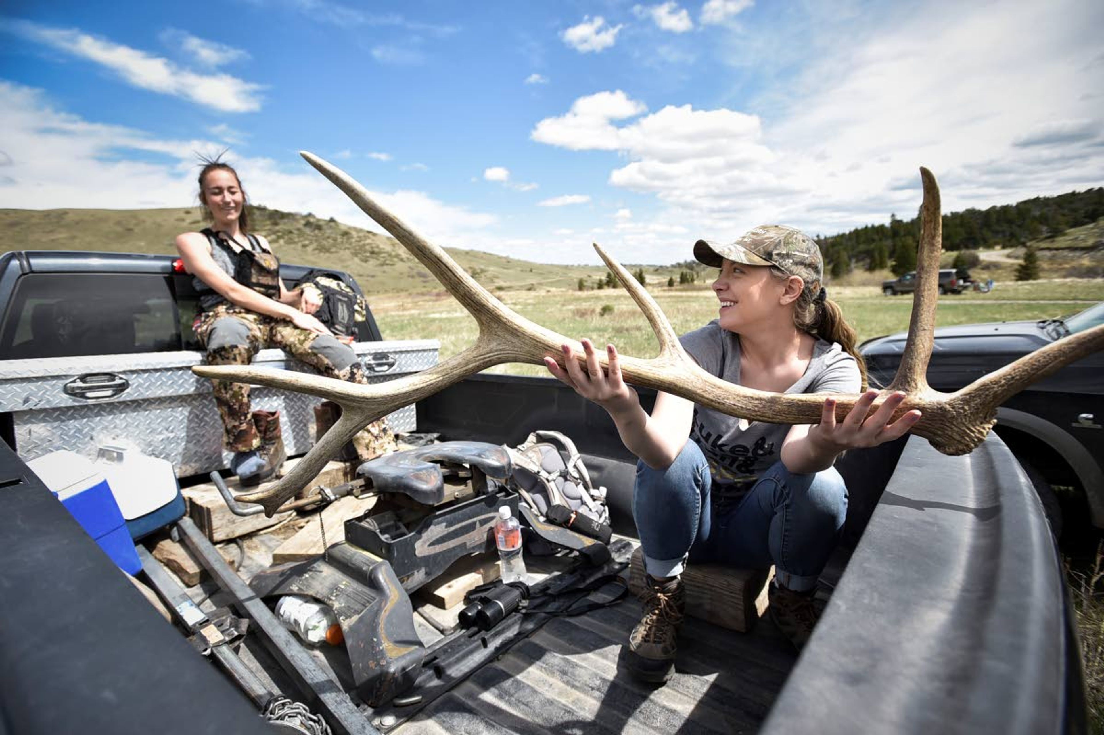 In this Wednesday, May 15, 2019 photo, Mariah Yates, right, and Bailee Pottratz laugh in the bed of a pickup after picking shed antlers at the Sun River Wildlife Management Area in Montana. (Thom Bridge/Independent Record via AP)