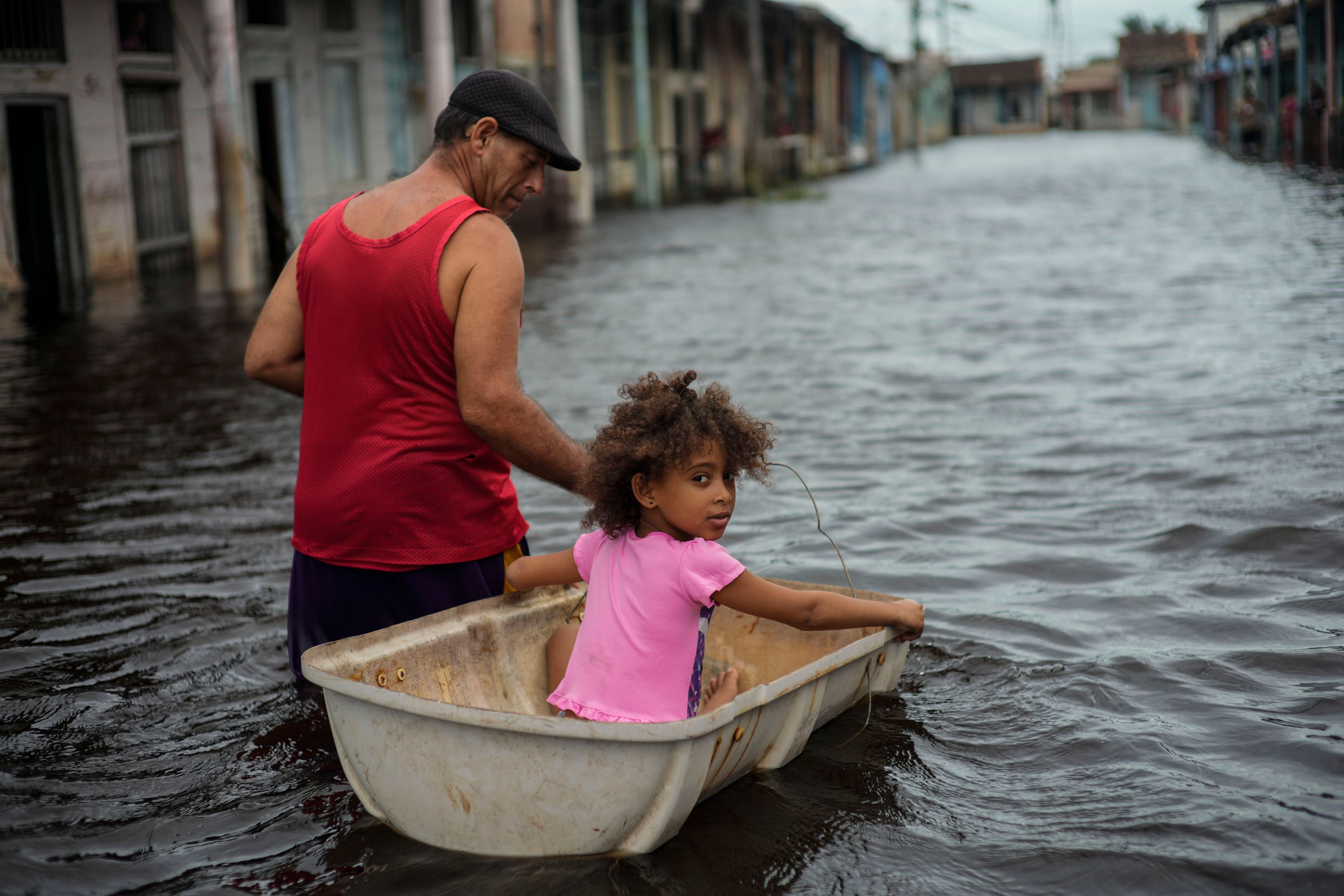 Jesus Hernandez guides his granddaughter Angelina via a container through a street flooded in the passing of Hurricane Helene, in Batabano, Mayabeque province, Cuba, Thursday, Sept. 26, 2024. (AP Photo/Ramon Espinosa)