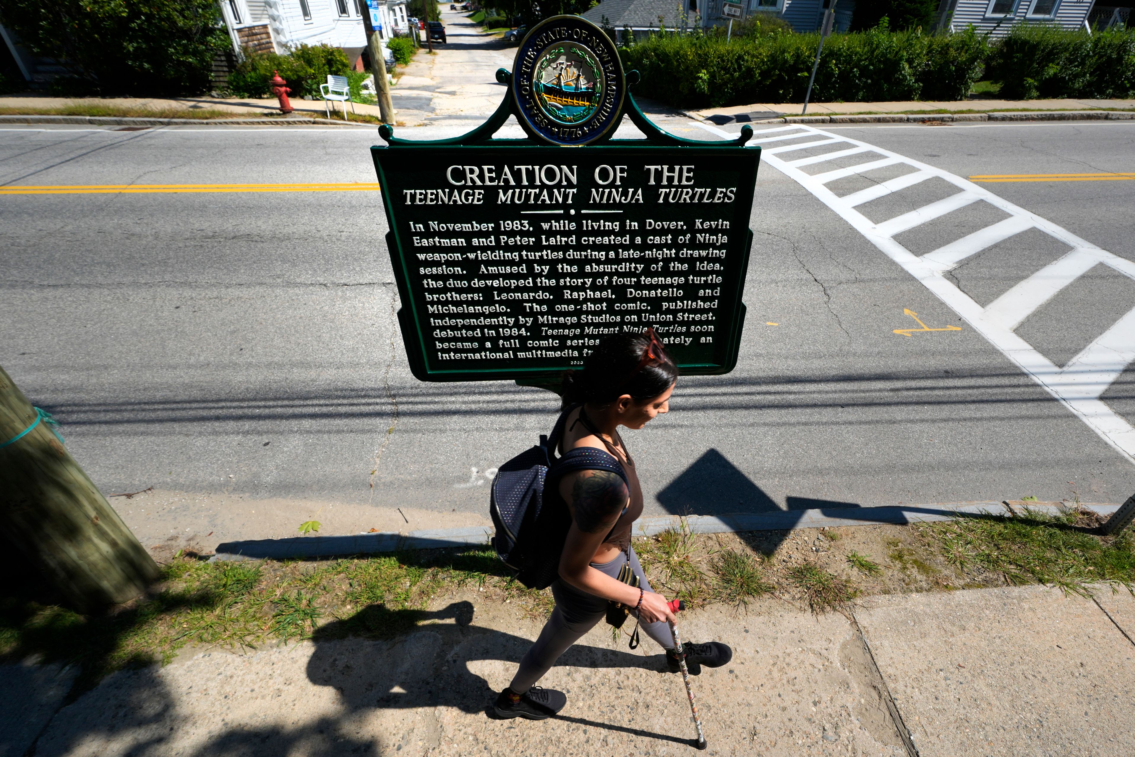 Heather Shingleton, of Dover, N.H., walks past a roadside marker honoring the local creation of the Teenage Mutant Ninja Turtles characters, Thursday, Sept. 5, 2024, in Dover.