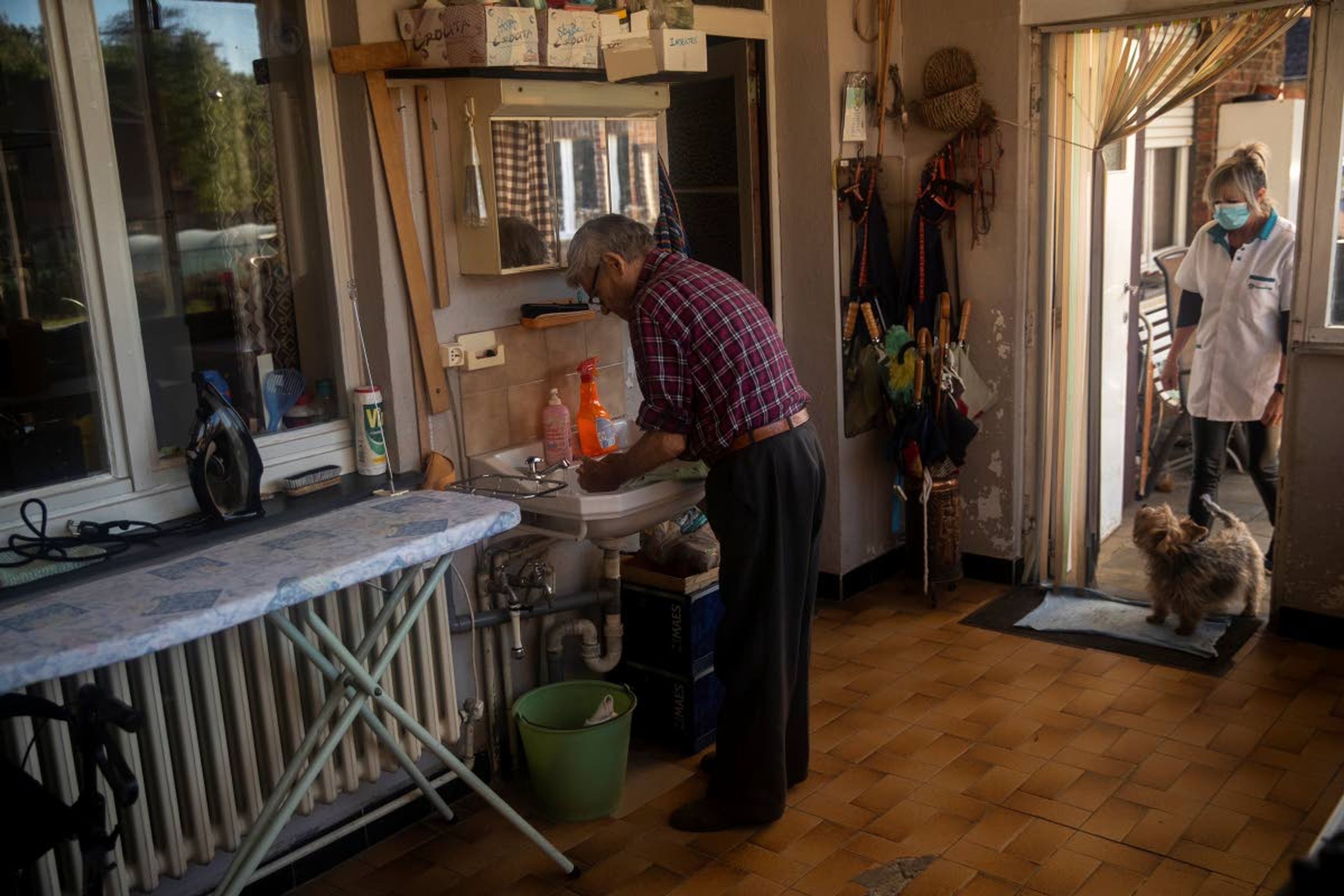 Familihulp home healthcare worker Nathalie Deroost, wears a face mask to protect against the spread of coronavirus, as she speaks with her client, former truck driver Jerome Demeyer, 86, at his house in Bierbeek, Belgium, Wednesday, May 6, 2020. Belgium is relaxing some of its lockdown measures Monday. Business-to-business companies can open their offices to employees again and those taking public transport must wear a mask. (AP Photo/Francisco Seco)