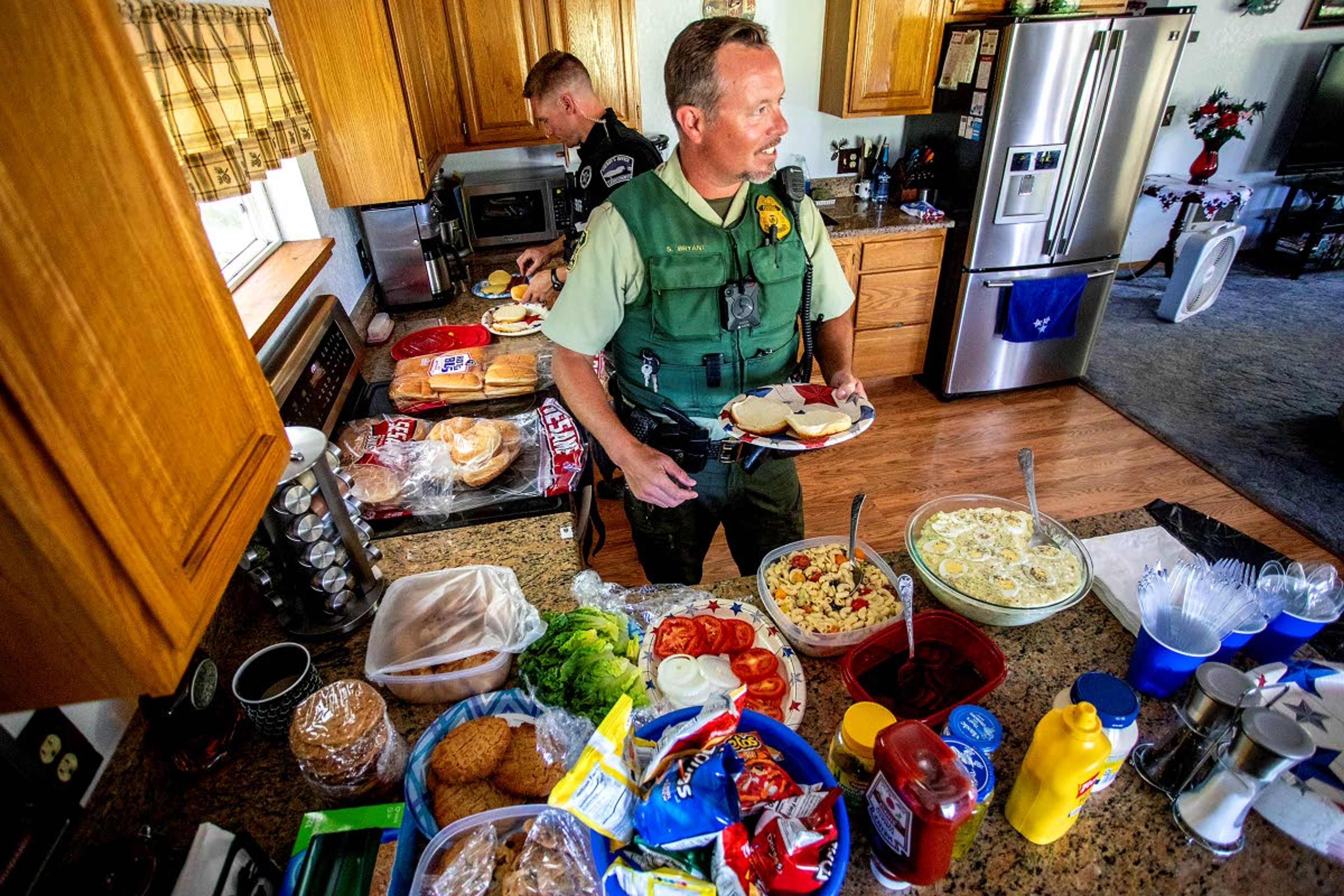 Steve Bryant, a law officer with the U.S. Forest Service, and Patrol Deputy Justin Olson (left) with the Latah County Sheriff’s Office, prepare to fill their plates for a meal Saturday at the Elk River home of Diana and Dave Olson. Bryant, Olson (no relation to their hosts) and other officers have a place to relax and eat a meal while they’re in town monitoring Fourth of July weekend activities in Elk River.