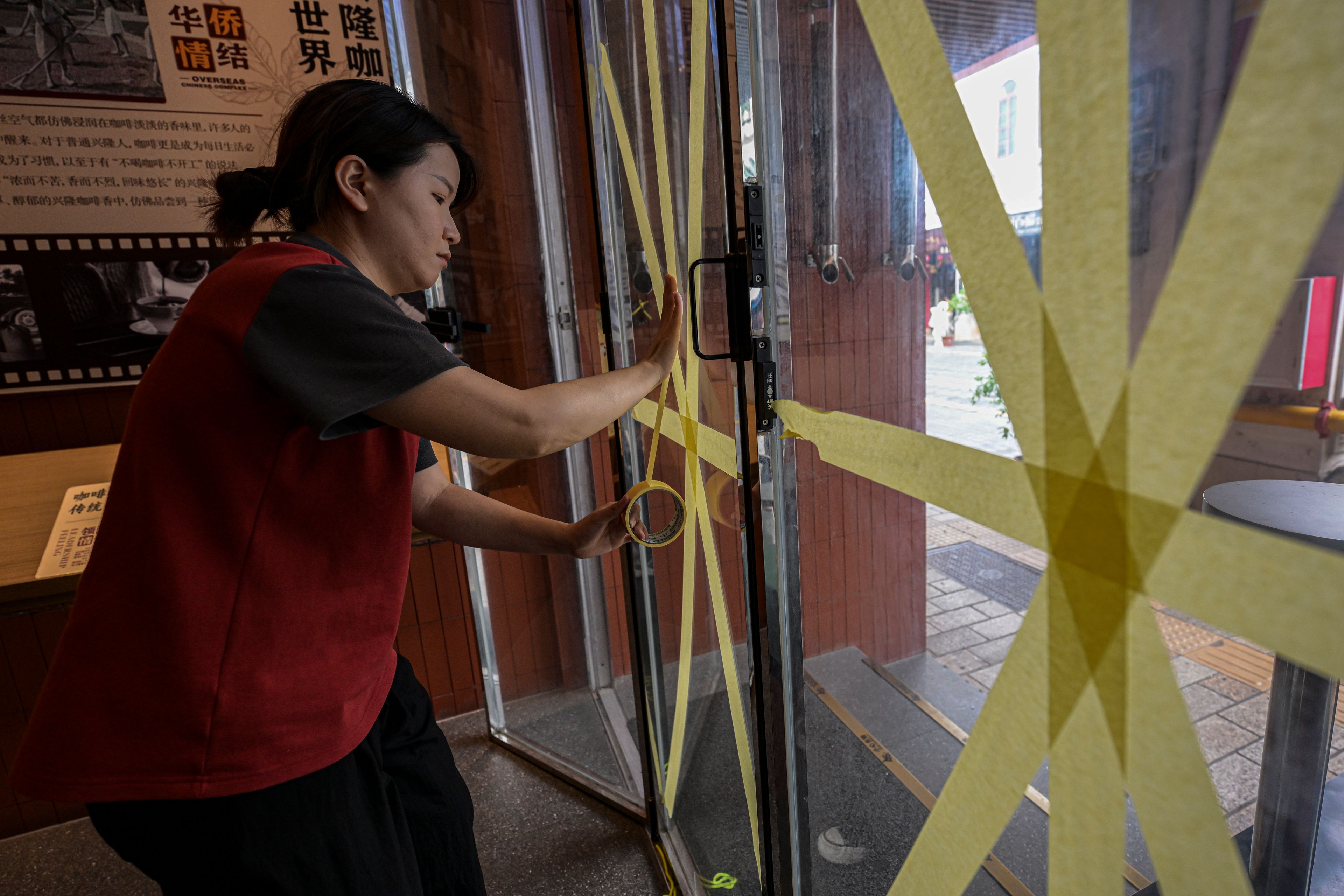 In this image released by Xinhua News Agency, a worker reinforces a glass window with tape at a cafe after the State Flood Control and Drought Relief Headquarters raised its emergency response for flood and typhoon prevention for Typhoon Yagi, Thursday, Sept. 5, 2024, in Haikou, south China's Hainan Province.