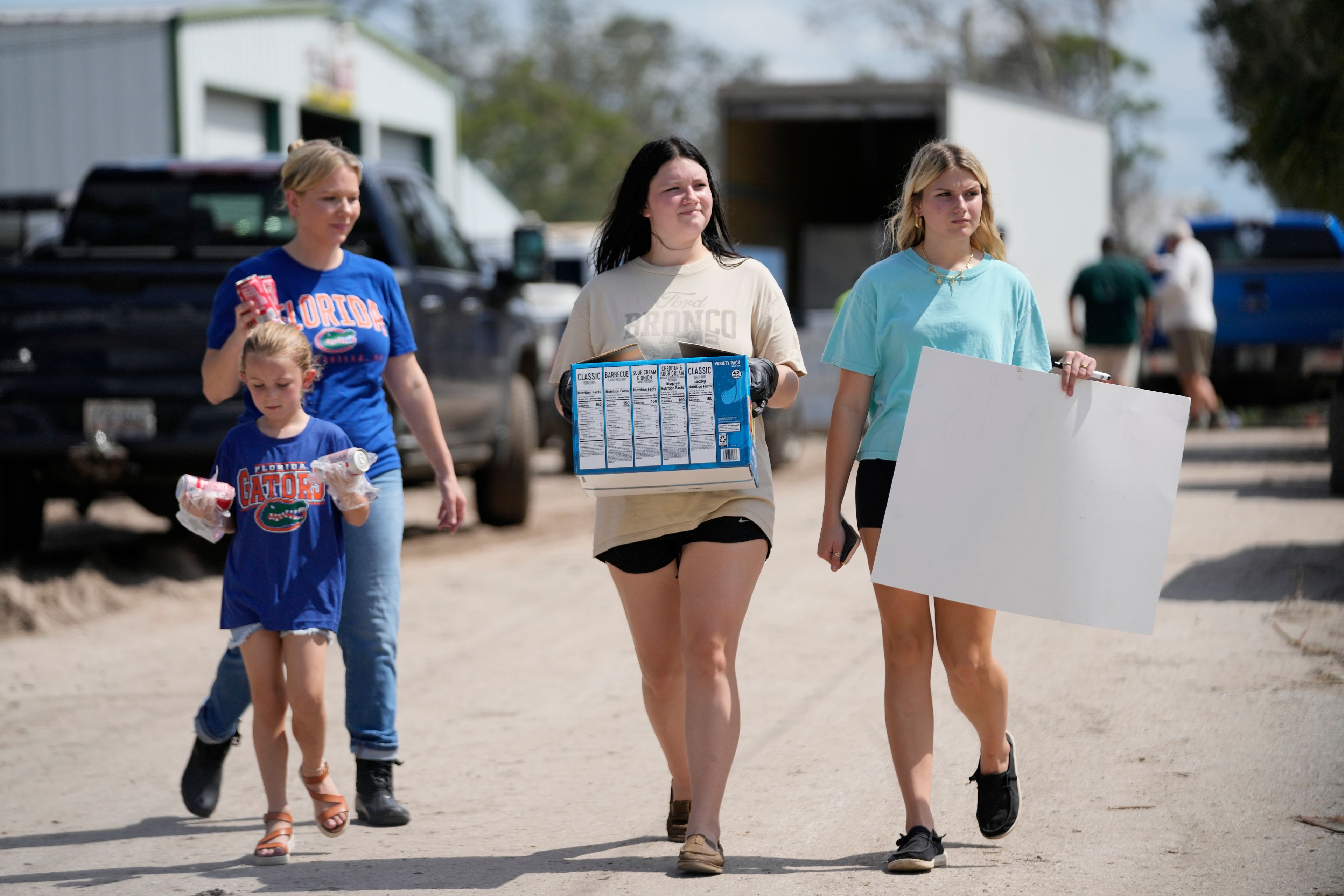 Volunteers Chelsea Marchant and her daughter Remi, along with Brennan Cordery, center, and Lynnlee Stratton, all of Dixie County, carry donations in the aftermath of Hurricane Helene, in Horseshoe Beach, Fla., Saturday, Sept. 28, 2024. (AP Photo/Gerald Herbert)