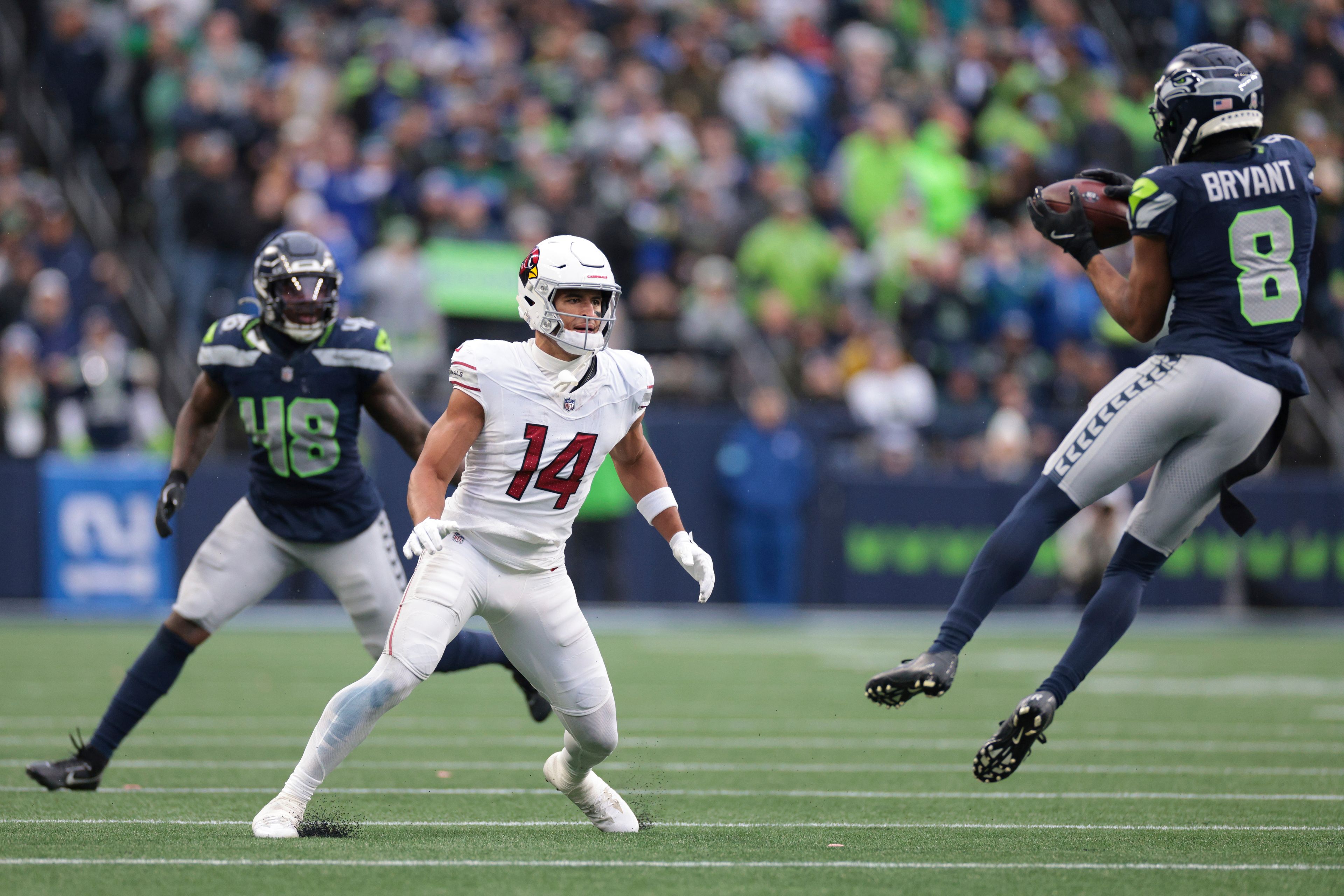 Arizona Cardinals wide receiver Michael Wilson (14) watches at Seattle Seahawks cornerback Coby Bryant (8) as he makes an interception during the second half of an NFL football game Sunday, Nov. 24, 2024, in Seattle. Bryant ran the ball in for a touchdown on the play. (AP Photo/Jason Redmond)