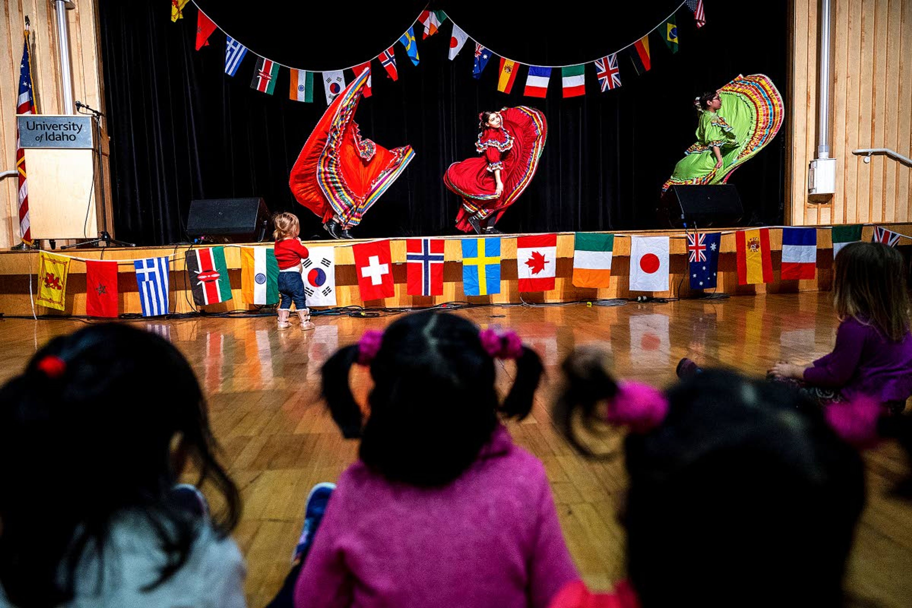 Children look on as Jessica Betancourt (left), Leslie Jimenez (center) and Melissa Galindo — all seniors at the University of Idaho — perform Jarape tapatio from Jalisco, Mexico during the Cruise the World event at the Pitman Center in Moscow on Saturday.