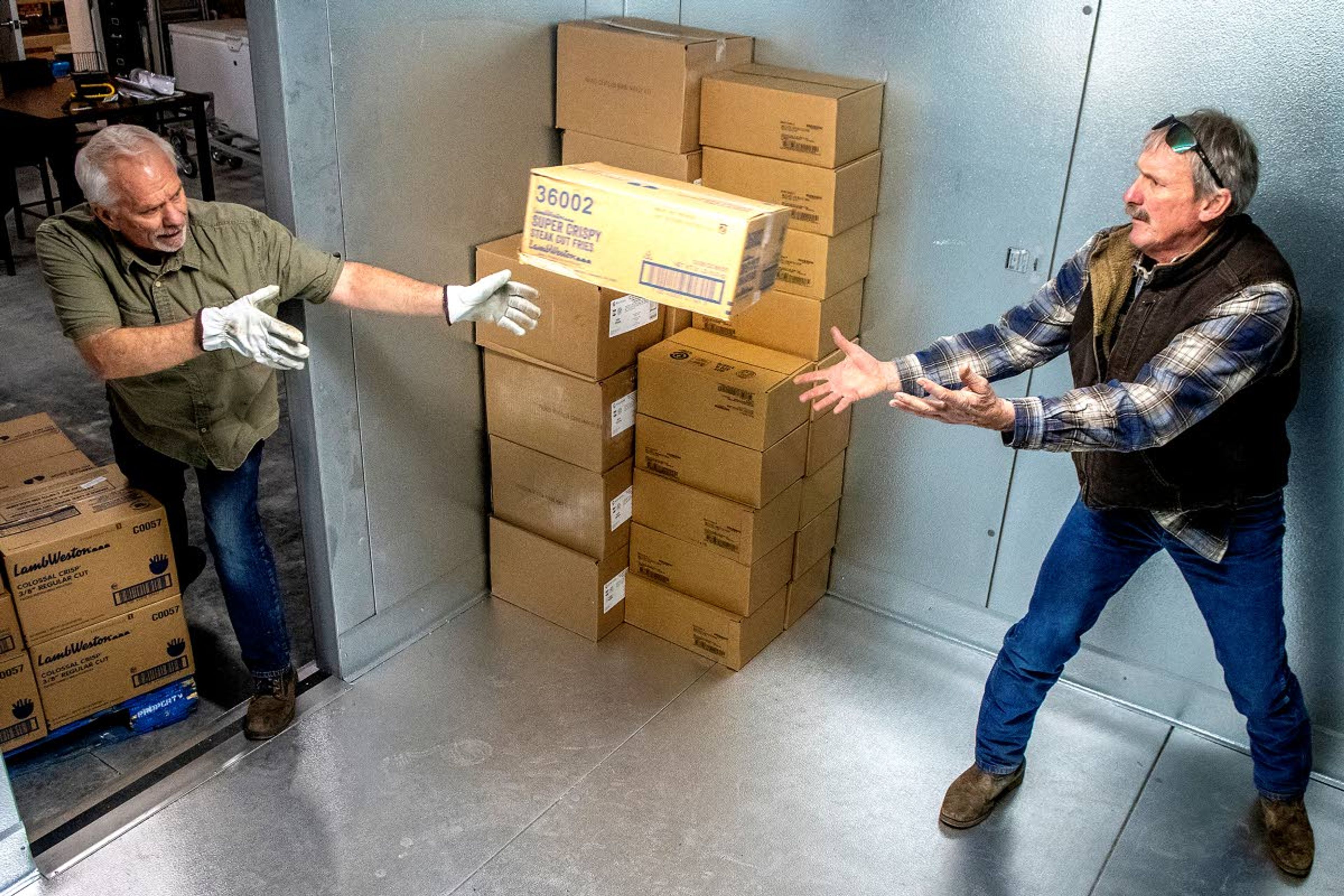 Ken Lefsaker (left) tosses a box of super crispy steak-cut fries to Jeff Goldman as they put the boxes away in the freezer at the new Camas Prairie Food Bank in Grangeville.