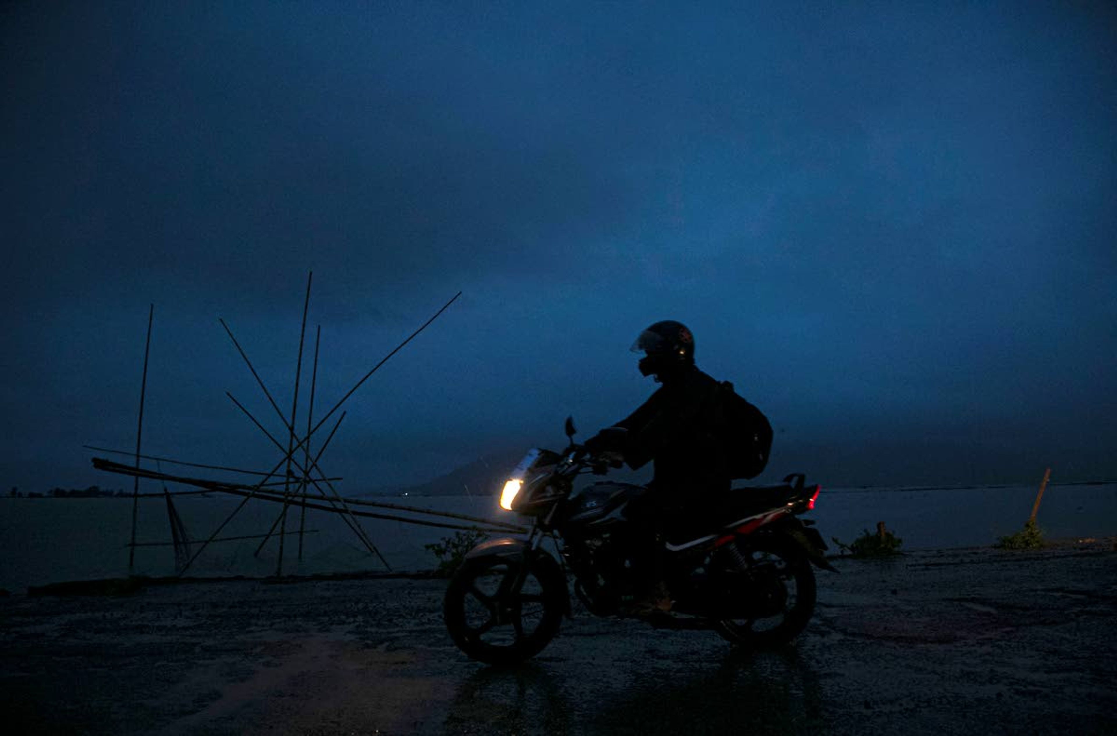 Ramananda Sarkar, 43, rides a bike towards his village to visit his family, early morning in Pobitora, in the notheastern Indian state of Assam, Tuesday, Sept. 22, 2020. While Hindu's believe cremation rights are sacred and release the dead person's soul from the cycle of rebirth, those who actually deal with corpses are looked down upon. After a month and a half of not seeing his wife and three sons, Sarkar snuck into his village in the middle of a recent rainy night. He called out to his family from the road outside his house and was able to spend 15 minutes with them and leave them some money. (AP Photo/Anupam Nath)