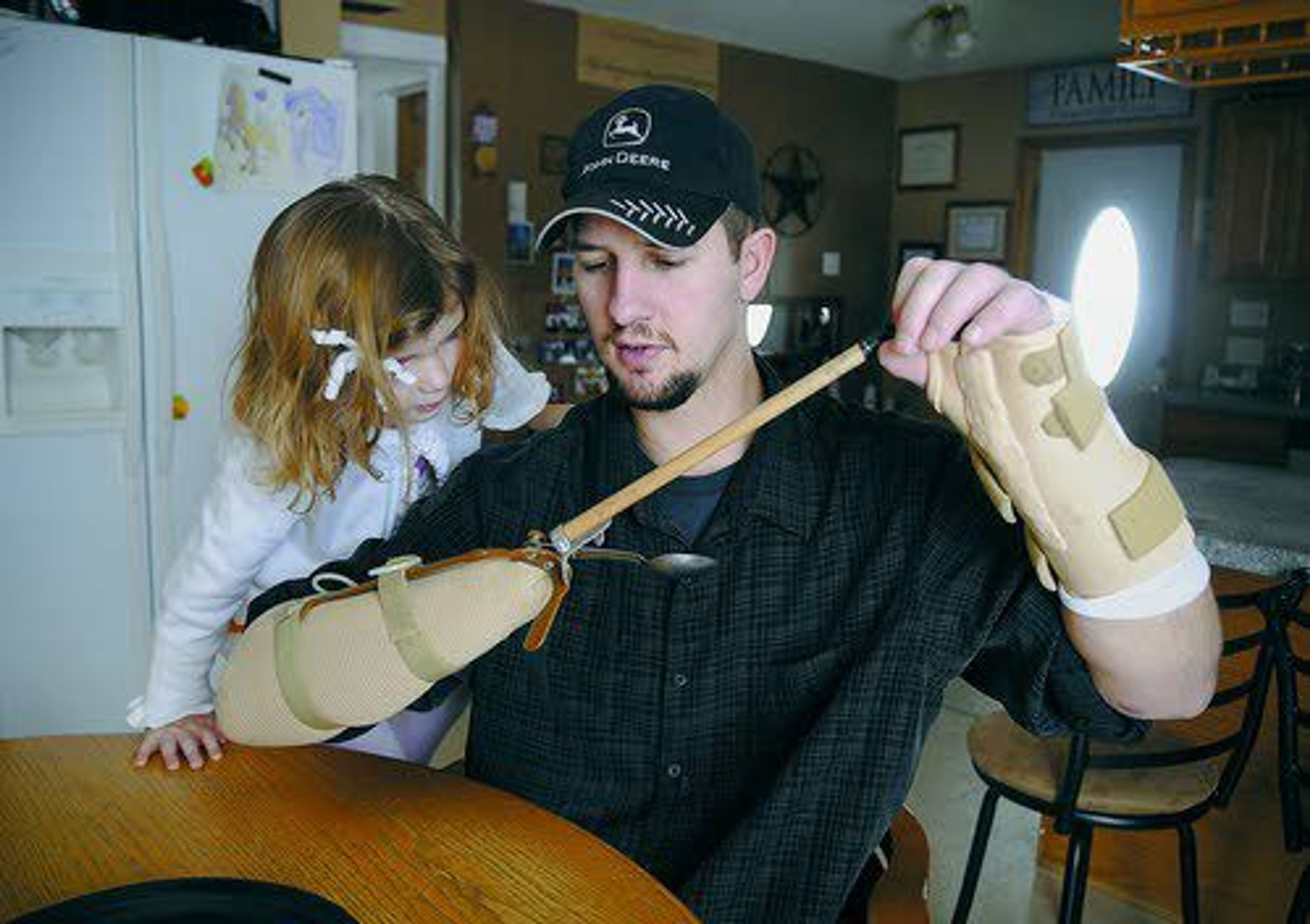 In this photograph taken Jan. 1, 2014, Madison Houdek watches as her father, Jamie, demonstrates tools he uses to eat and use a computer tablet since losing his right hand to a corn picker in November 2013 on the 60-acre hobby farm where he raises beef cattle near Little Falls, Minn.