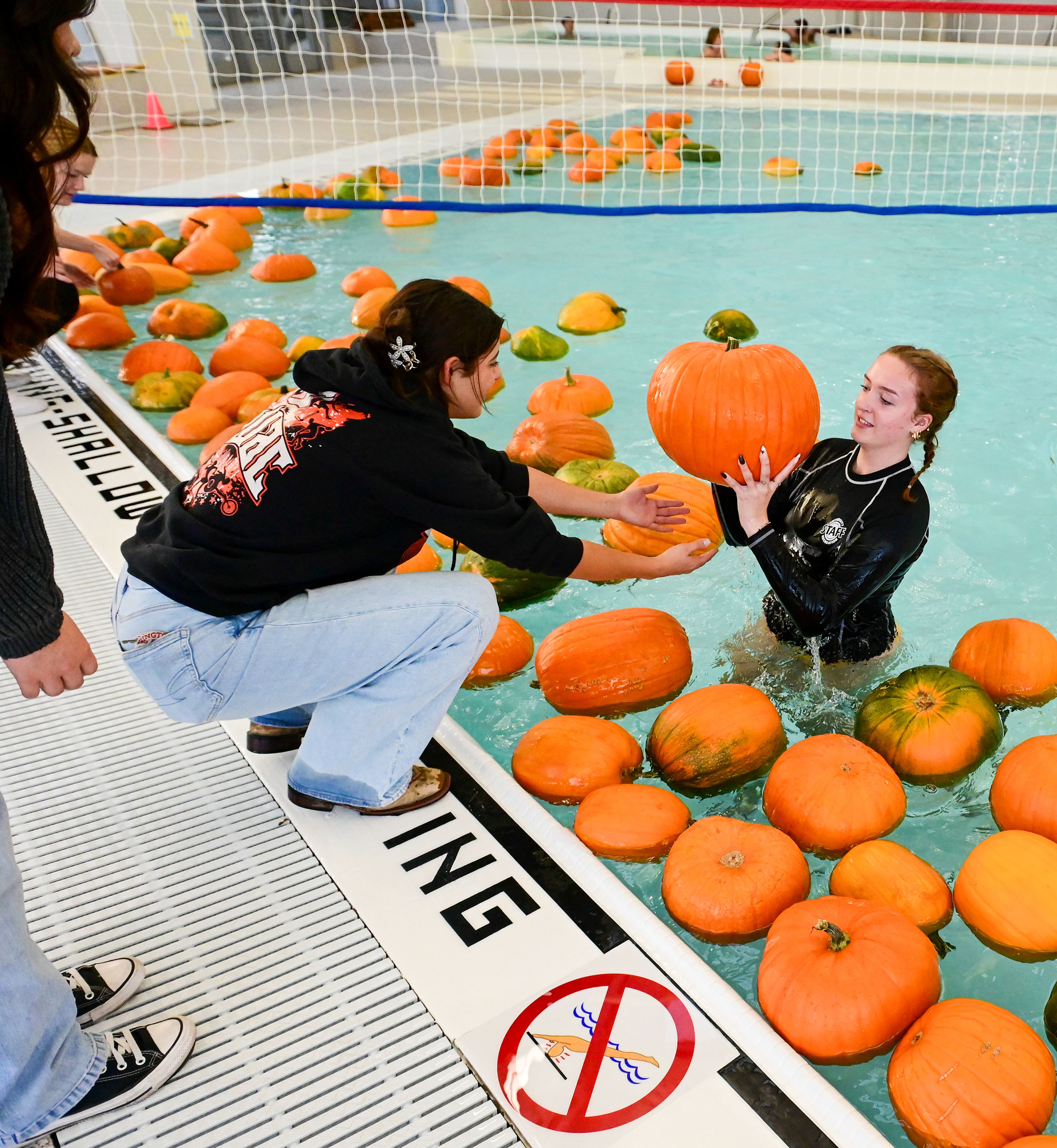 First year Abby Toro is handed a pumpkin by lifeguard and sophomore Elaina Peloquin, right, from the AquaPatch at the WSU Student Recreation Center Wednesday in Pullman.,