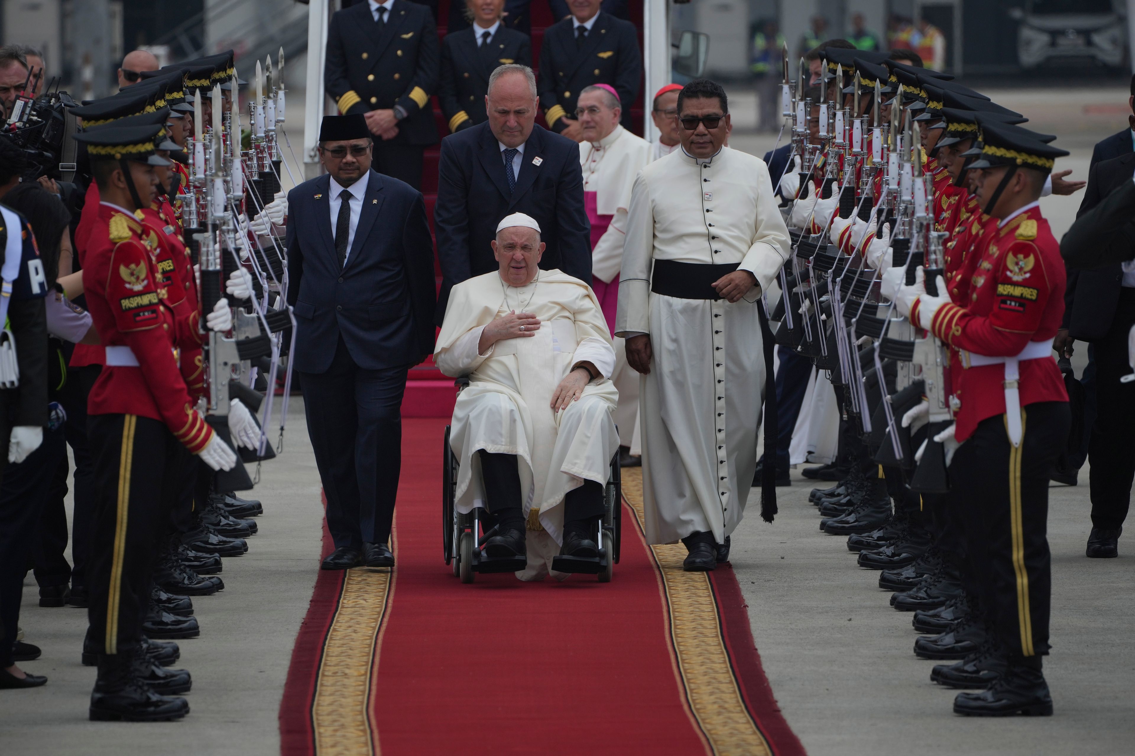 Pope Francis on his wheelchair, is welcomed as Indonesian Minister of Religious Affairs Yaqut Cholil Qoumas, center left, walks during an official welcoming ceremony at Soekarno-Hatta International Airport in Tangerang on the outskirts of Jakarta, Indonesia, Tuesday, Sept. 3, 2024.