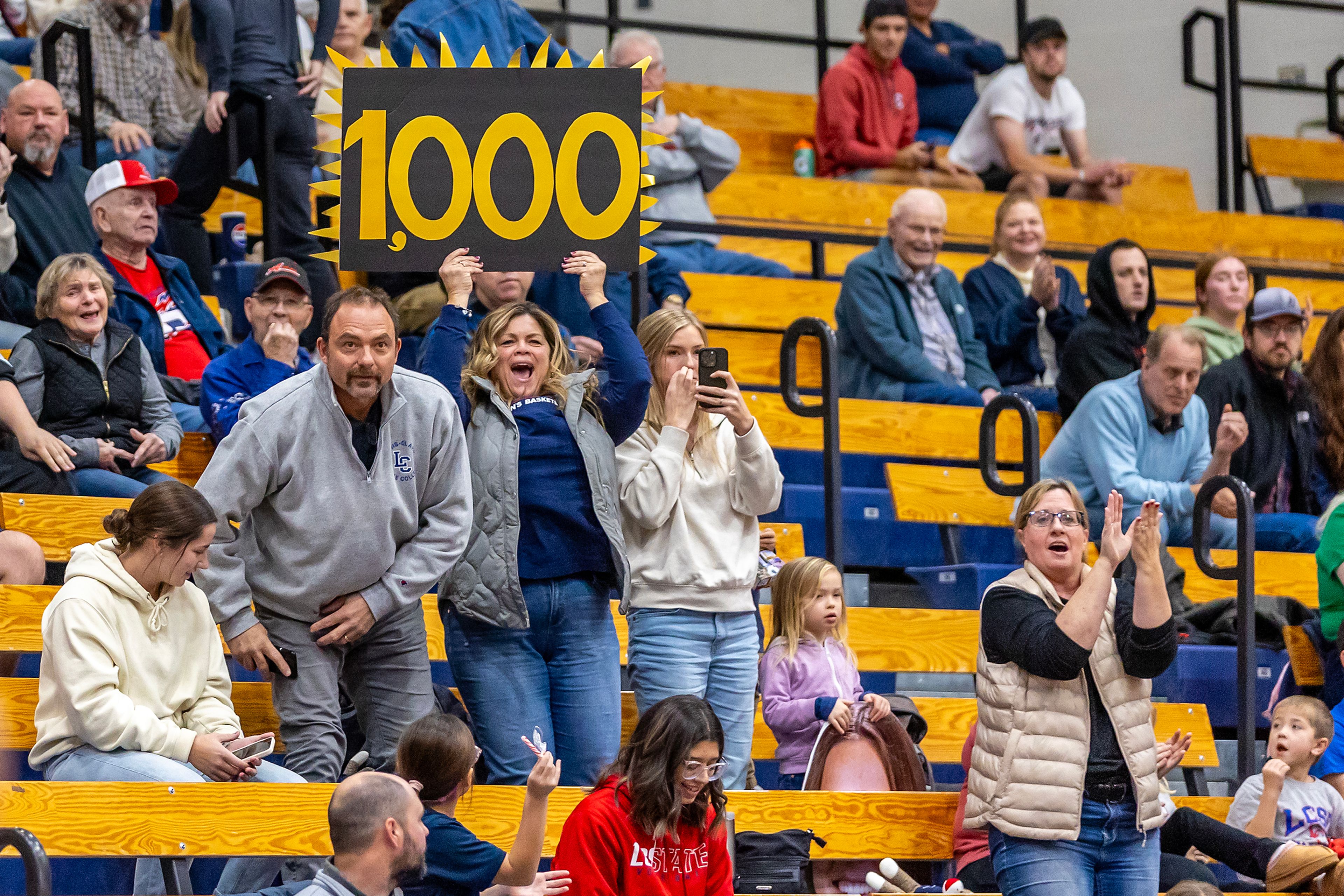 Ellie Sander’s parents hold up a sign celebrating Sander’s 1,000th point during a Cascade Conference game Tuesday at Lewis-Clark State College in Lewiston.