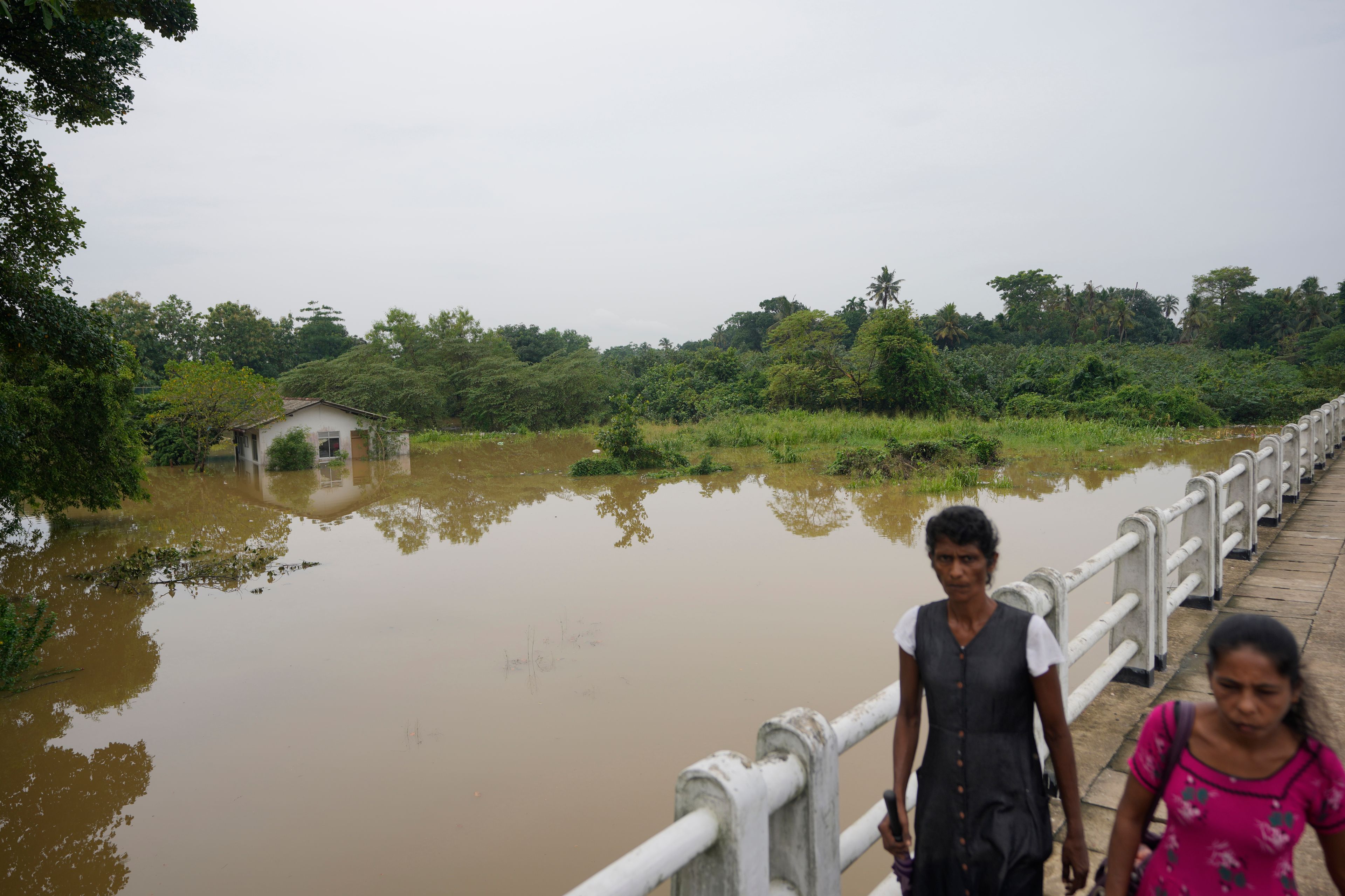 People walk over a bridge in a submerged area in Kelaniya, a suburb of Colombo, Sri Lanka, Monday, June 3, 2024. Sri Lanka closed schools on Monday as heavy rains triggered floods and mudslides in many parts of the island nation, killing at least 10 people while six others have gone missing, officials said.