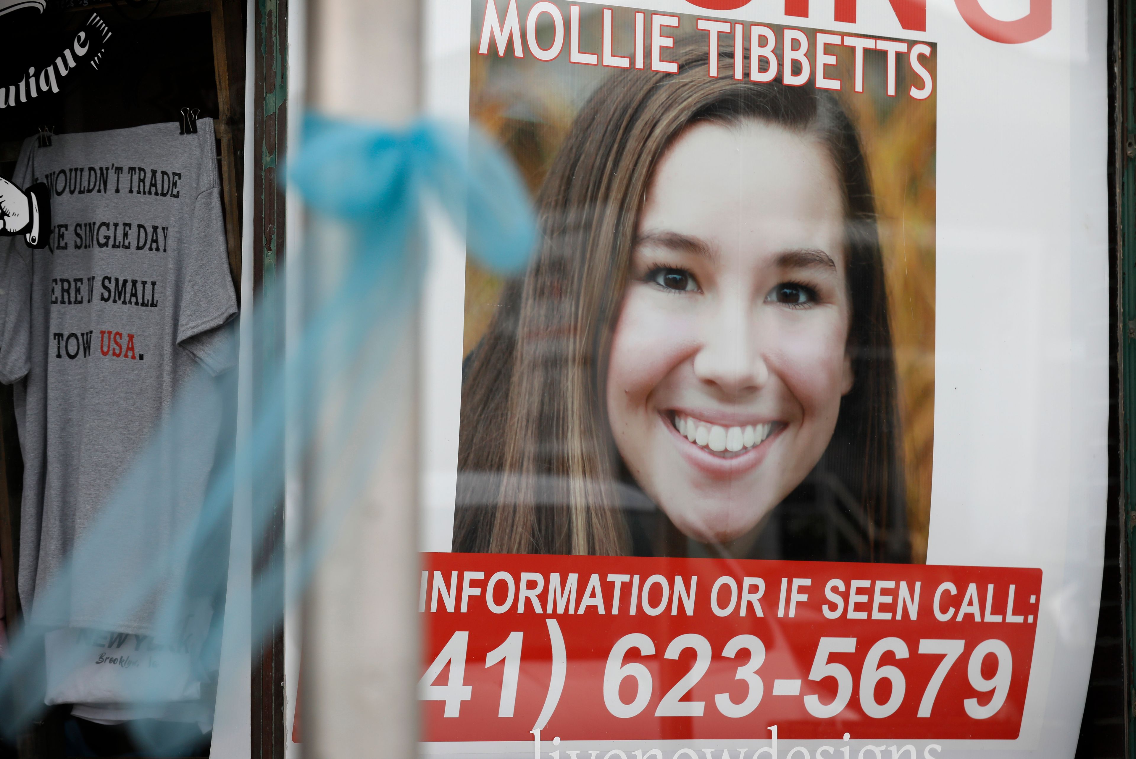 FILE - In this Aug. 21, 2018, file photo, a poster for then missing University of Iowa student Mollie Tibbetts hangs in the window of a local business in Brooklyn, Iowa. Regulators are proposing a nearly $13 million fine against Scott Rhodes, who they say illegally hid the origin of automated phone calls that used the slaying of Tibbetts, and election campaigns in other states to promote white nationalist and anti-Semitic messages. The Federal Communications Commission said in a news release Thursday, Jan. 30, 2020, Rhodes violated the Truth in Caller ID Act, which bars the manipulation of caller ID information. (AP Photo/Charlie Neibergall, File)