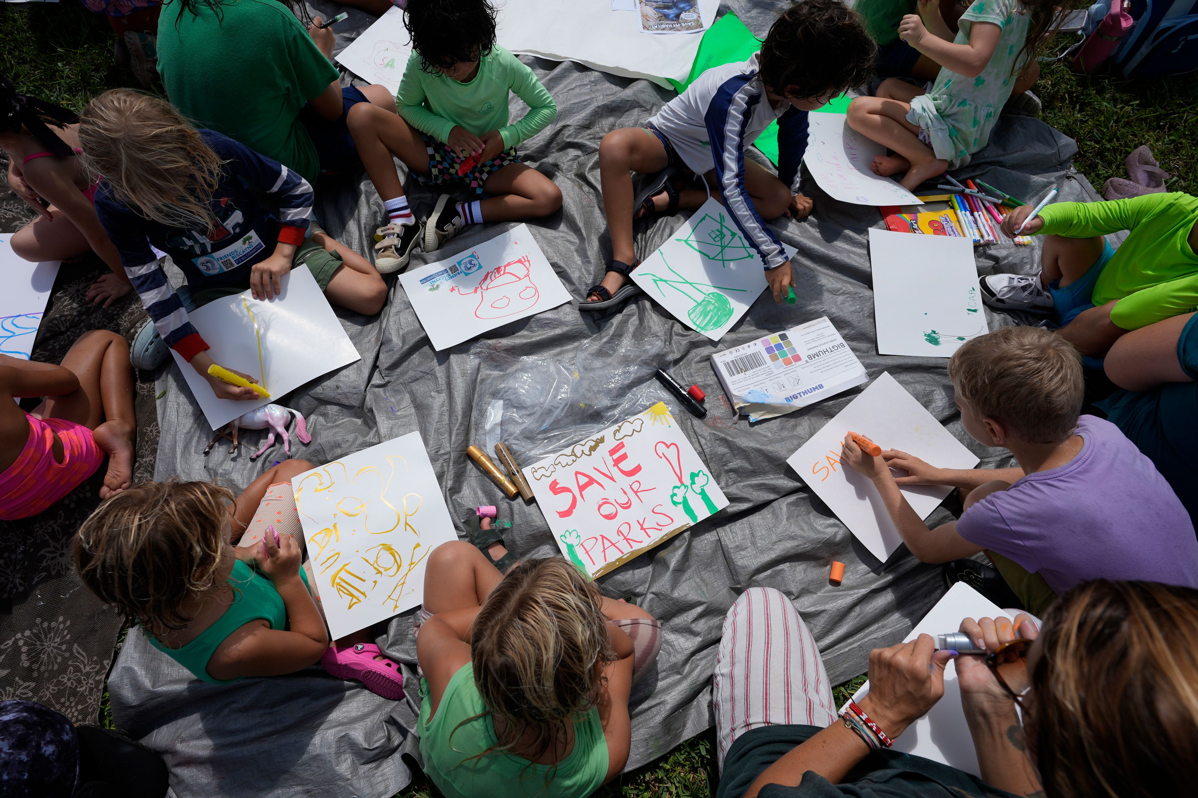 Children make signs as they attend a protest against Gov. Ron DeSantis' plan to develop state parks with business ventures such as golf courses, pickleball courts and large hotels, during a demonstration at Oleta River State Park, Tuesday, Aug. 27, 2024, in North Miami Beach, Fla.