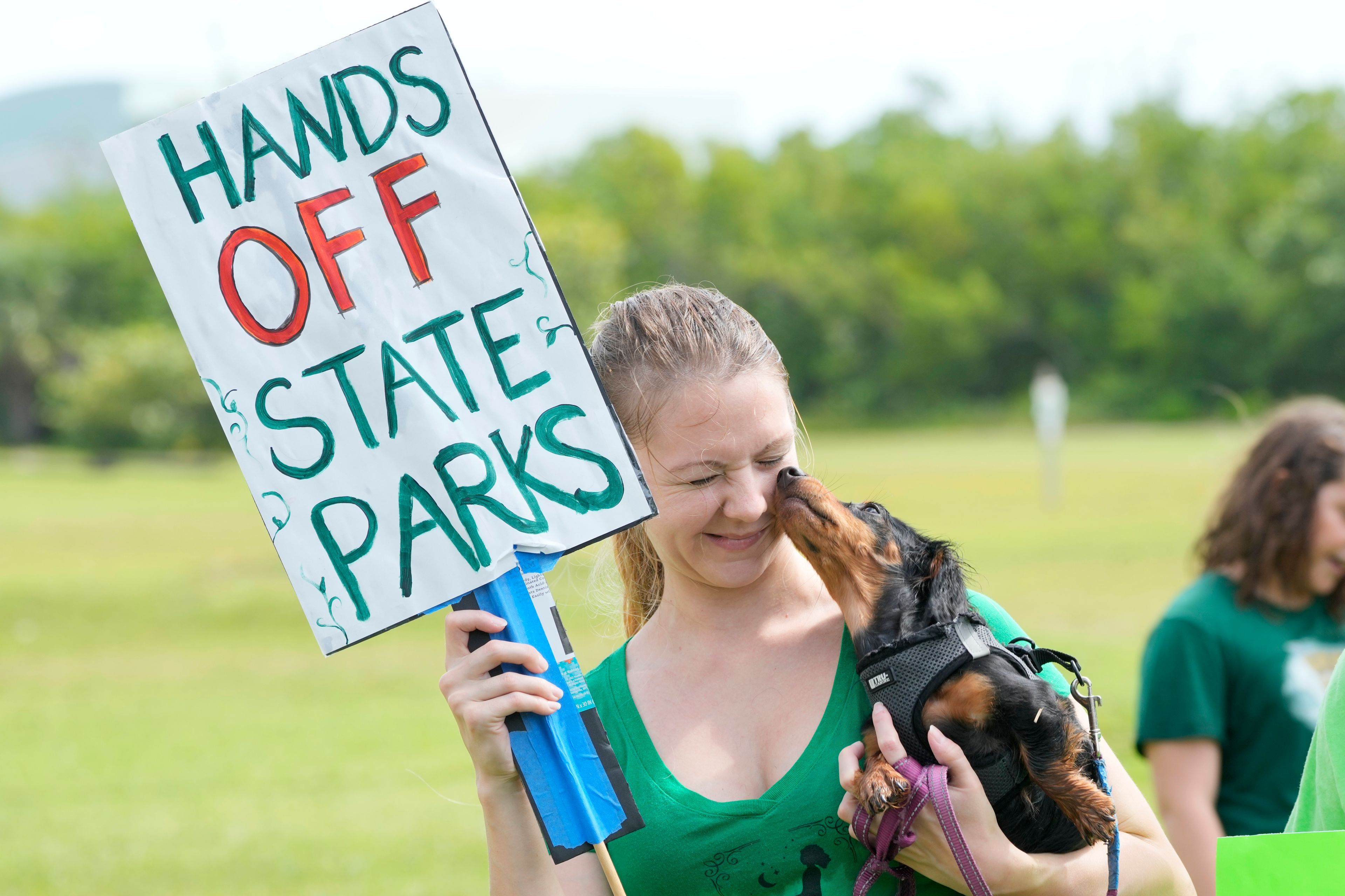 Bonnie, a seven-month-old dachshund, licks Alexandra Maxwell's face as they a protest against Gov. Ron DeSantis' plan to develop state parks with business ventures such as golf courses, pickleball courts and large hotels, during a demonstration at Oleta River State Park, Tuesday, Aug. 27, 2024, in North Miami Beach, Fla.