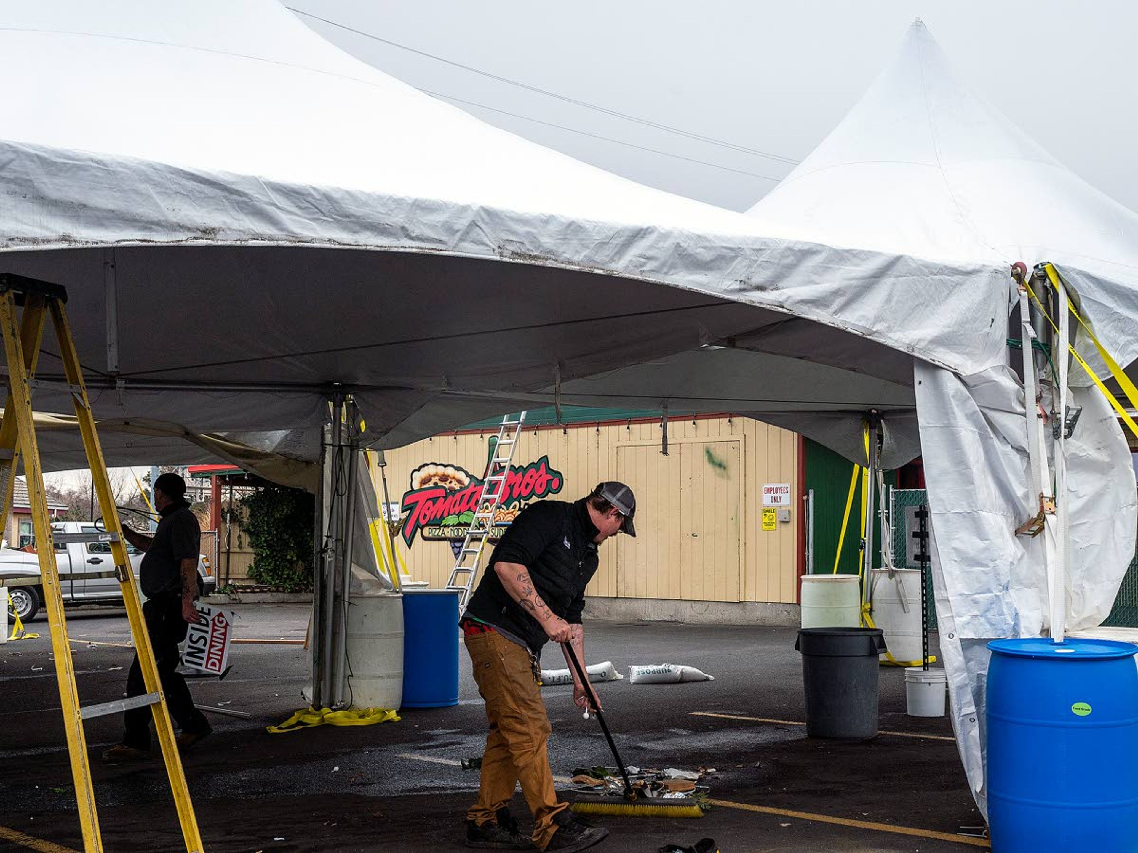 Happy Day Restaurants maintenance crew members Paul Thomas (left) and Tim Kelly clean up the tent seating area behind Tomato Bros on Monday afternoon in Clarkston. The restaurant is in the process of taking down its tents despite still having a 25 percent capacity cap on inside dining. The restaurant is hoping the state government will increase capacity levels for restaurants in Washington in the next couple of weeks.