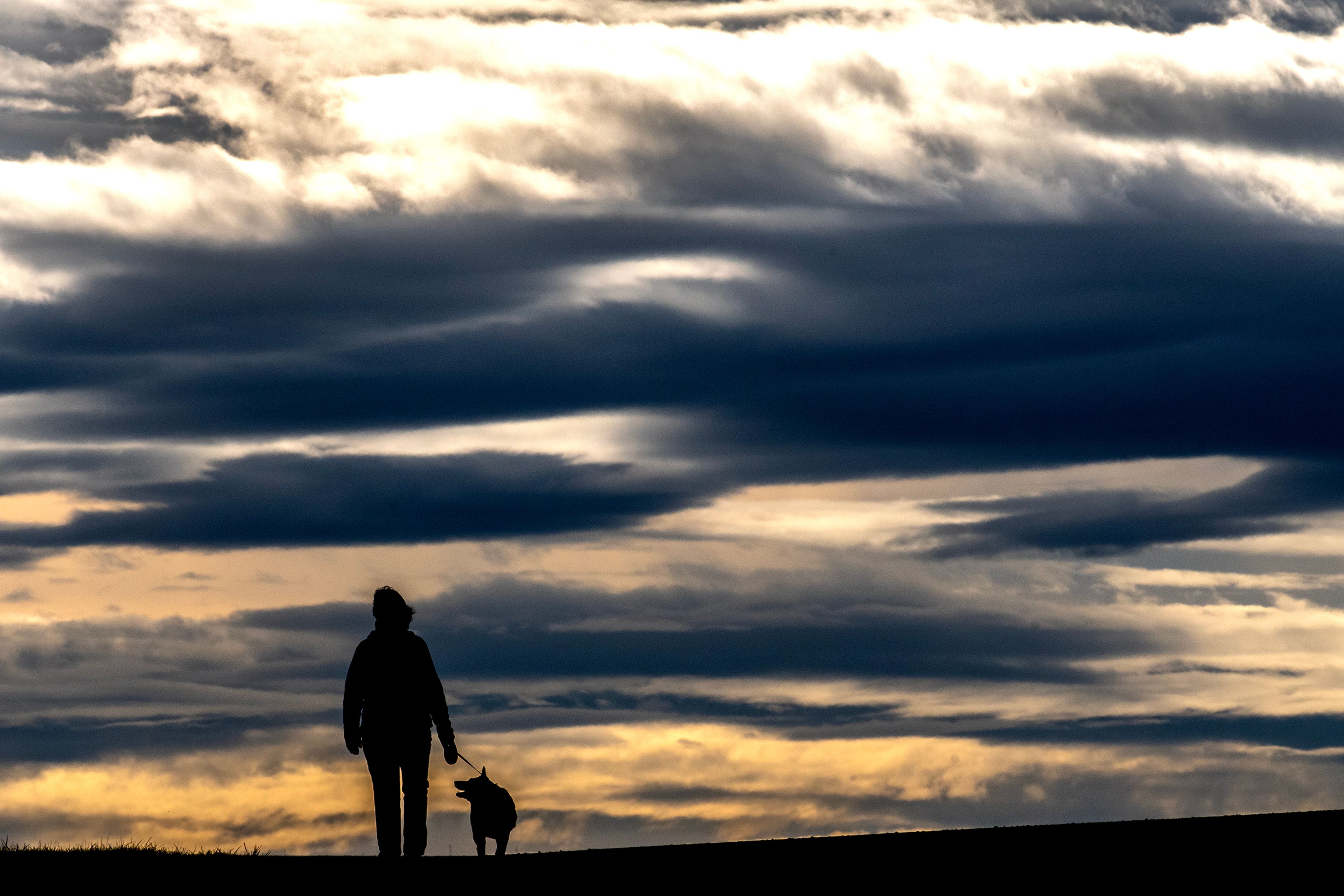 A dog walker moves down the Lewiston Levee Parkway Trail as sun shines through layers of clouds in the distance on Tuesday.