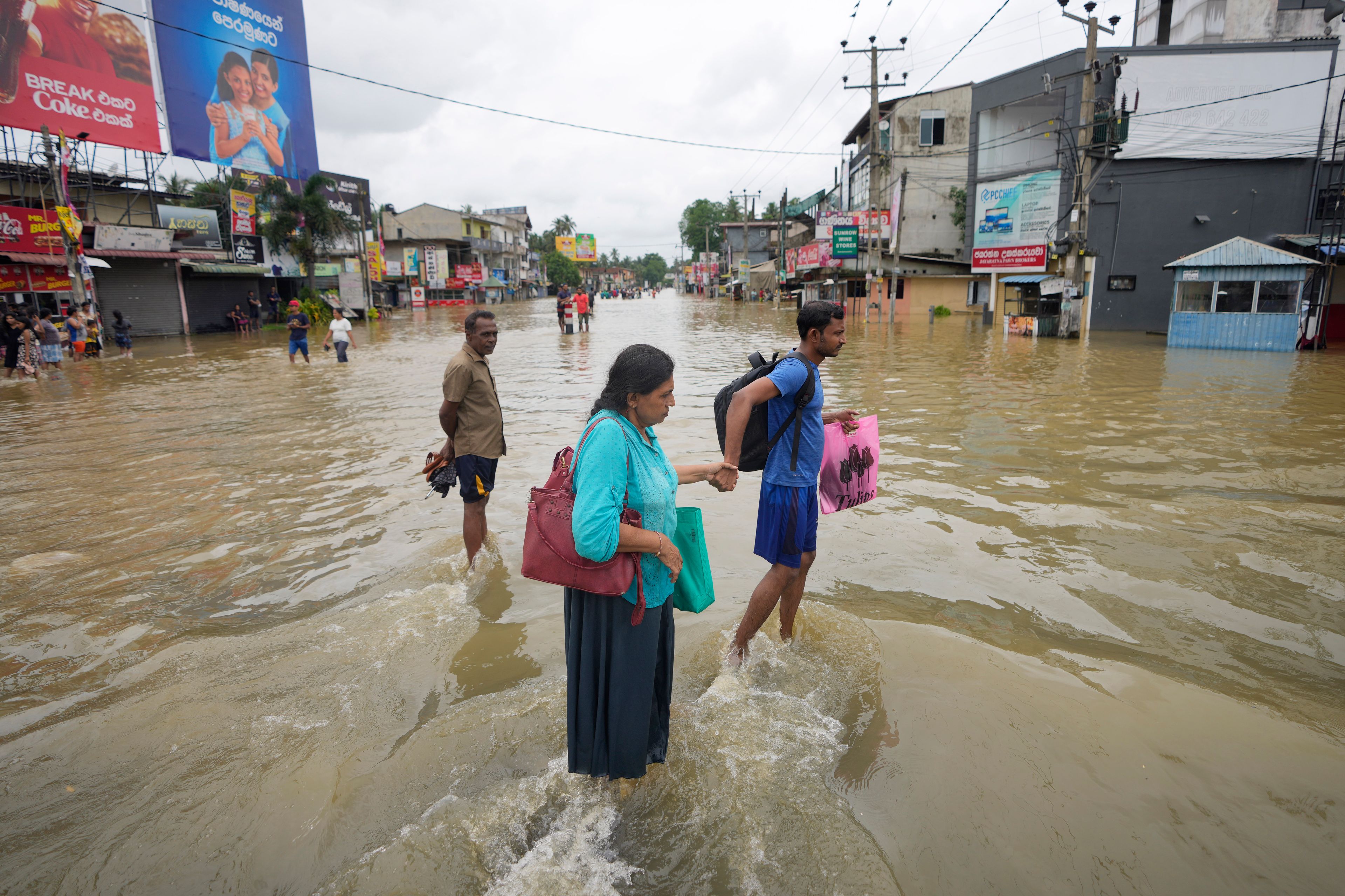 People wade through a flooded street in Biyagama, a suburb of Colombo, Sri Lanka, Monday, Jun. 3, 2023. Sri Lanka closed schools on Monday as heavy rains triggered floods and mudslides in many parts of the island nation, killing at least 10 people while six others have gone missing, officials said.