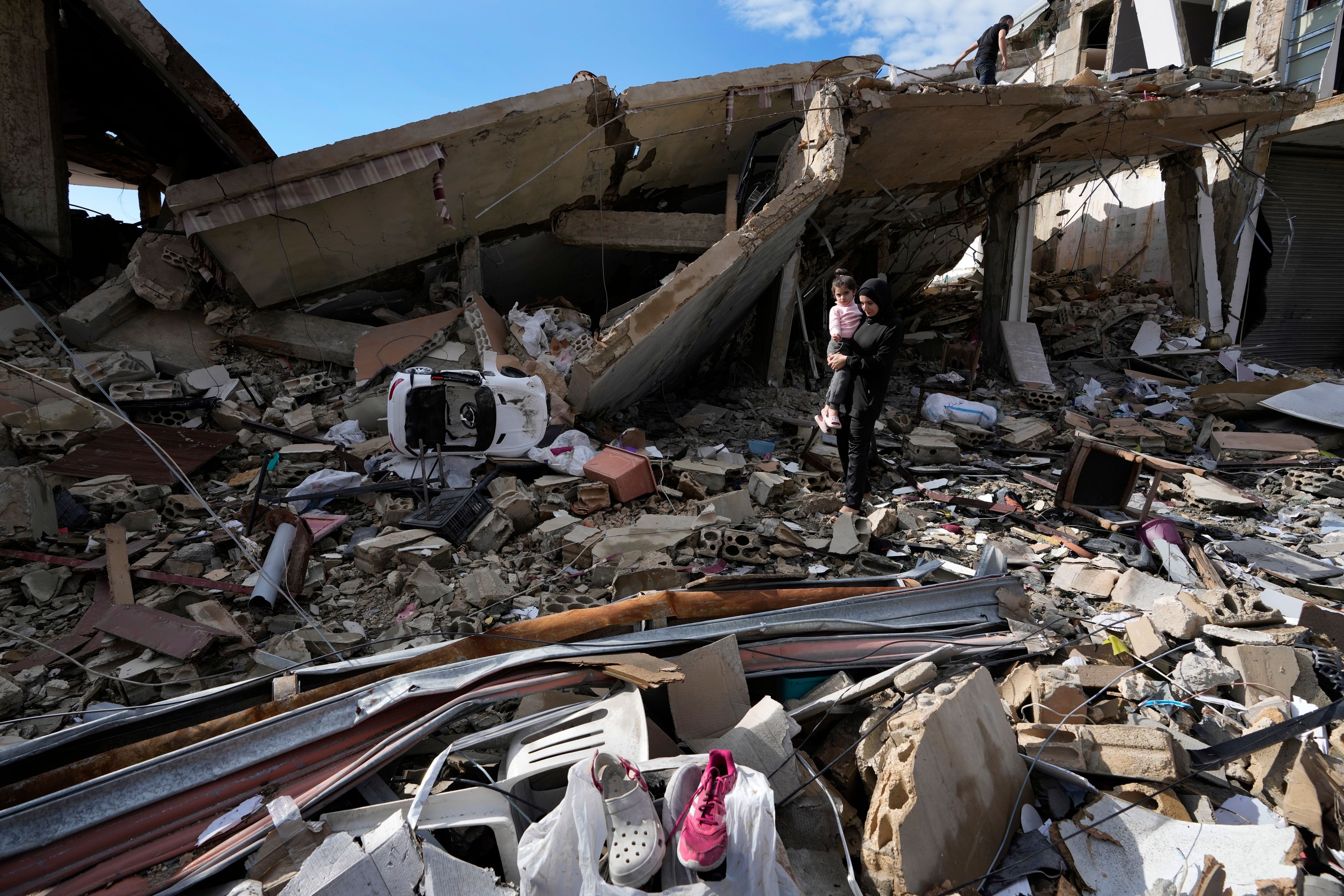 Safaa Haidous, carries her daughter Yara, 4, while walking on the rubble of her parents destroyed house after she returned to Hanouiyeh village, southern Lebanon, Thursday, Nov. 28, 2024 following a ceasefire between Israel and Hezbollah that went into effect on Wednesday.(AP Photo/Hussein Malla)