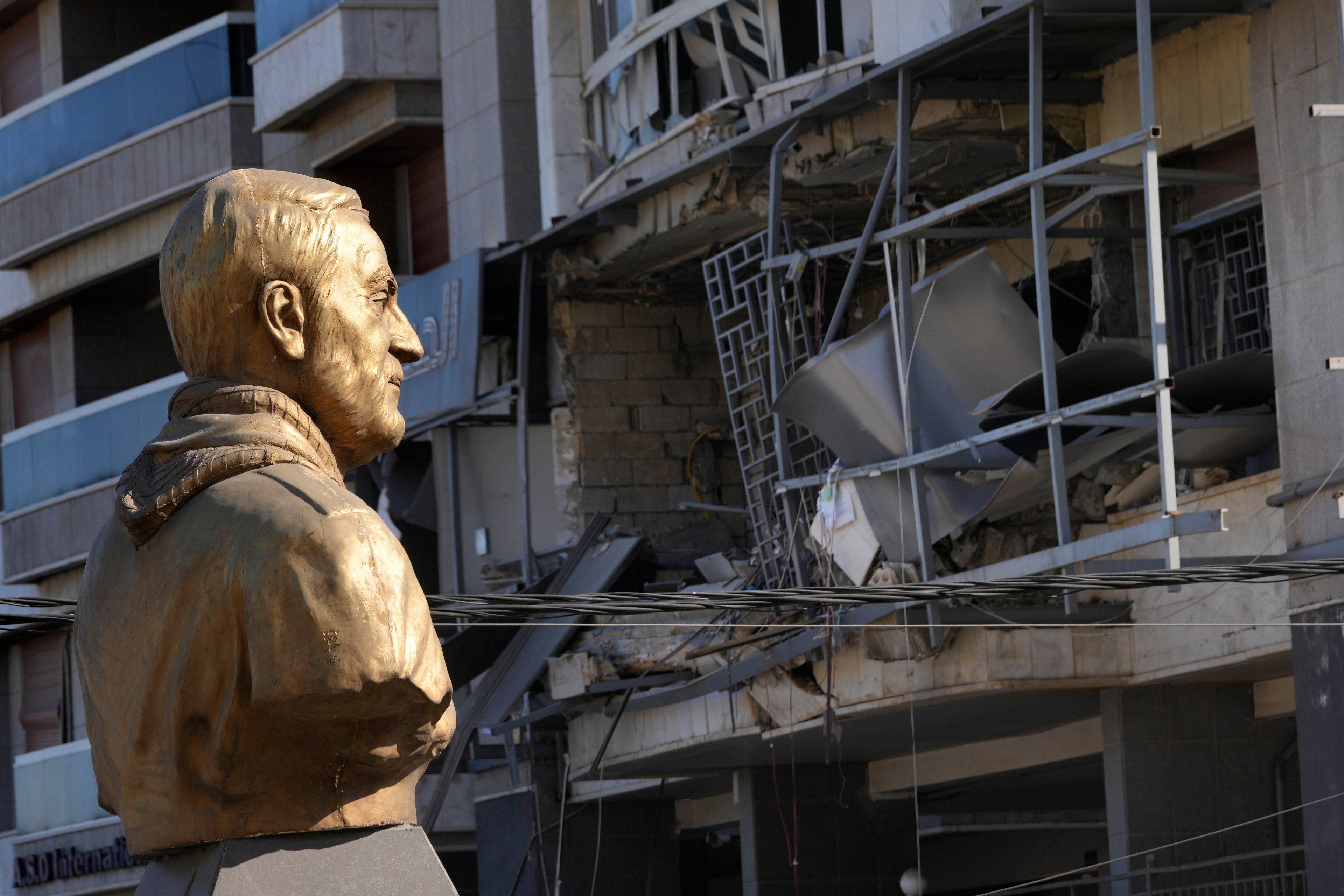 A bust of the late Iranian General Qassem Soleimani stands in front of a destroyed branch of the Hezbollah-run Qard al-Hassan, which was hit by an Israeli airstrike in Dahiyeh, Beirut, Lebanon, Monday, Oct. 21, 2024. (AP Photo/Hussein Malla)