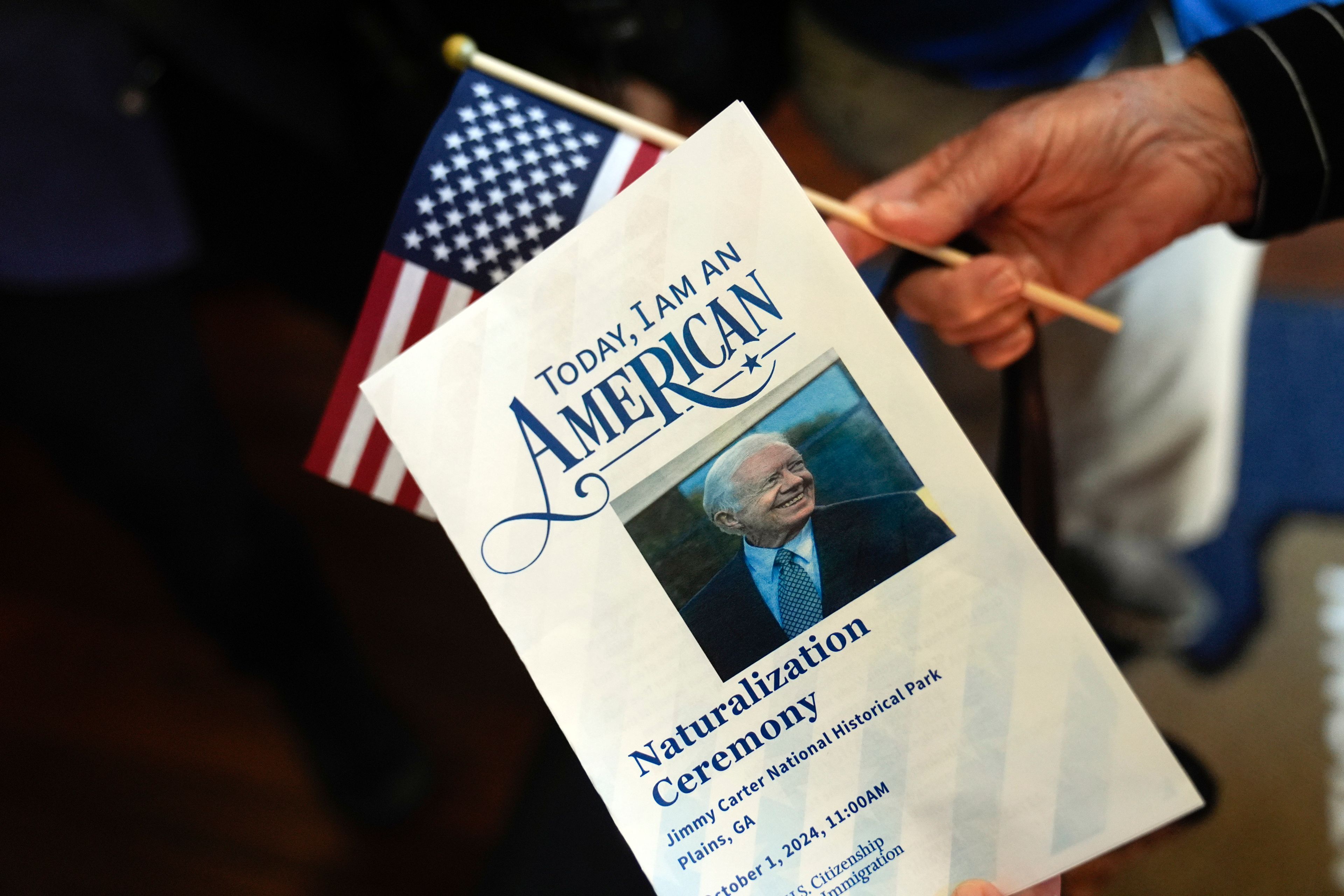 A person holds a program after a naturalization ceremony one hundred people to become U.S. citizens at the high school attended by former President Jimmy Carter on Carter's 100th birthday Tuesday, Oct. 1, 2024, in Plains, Ga. (AP Photo/John Bazemore)