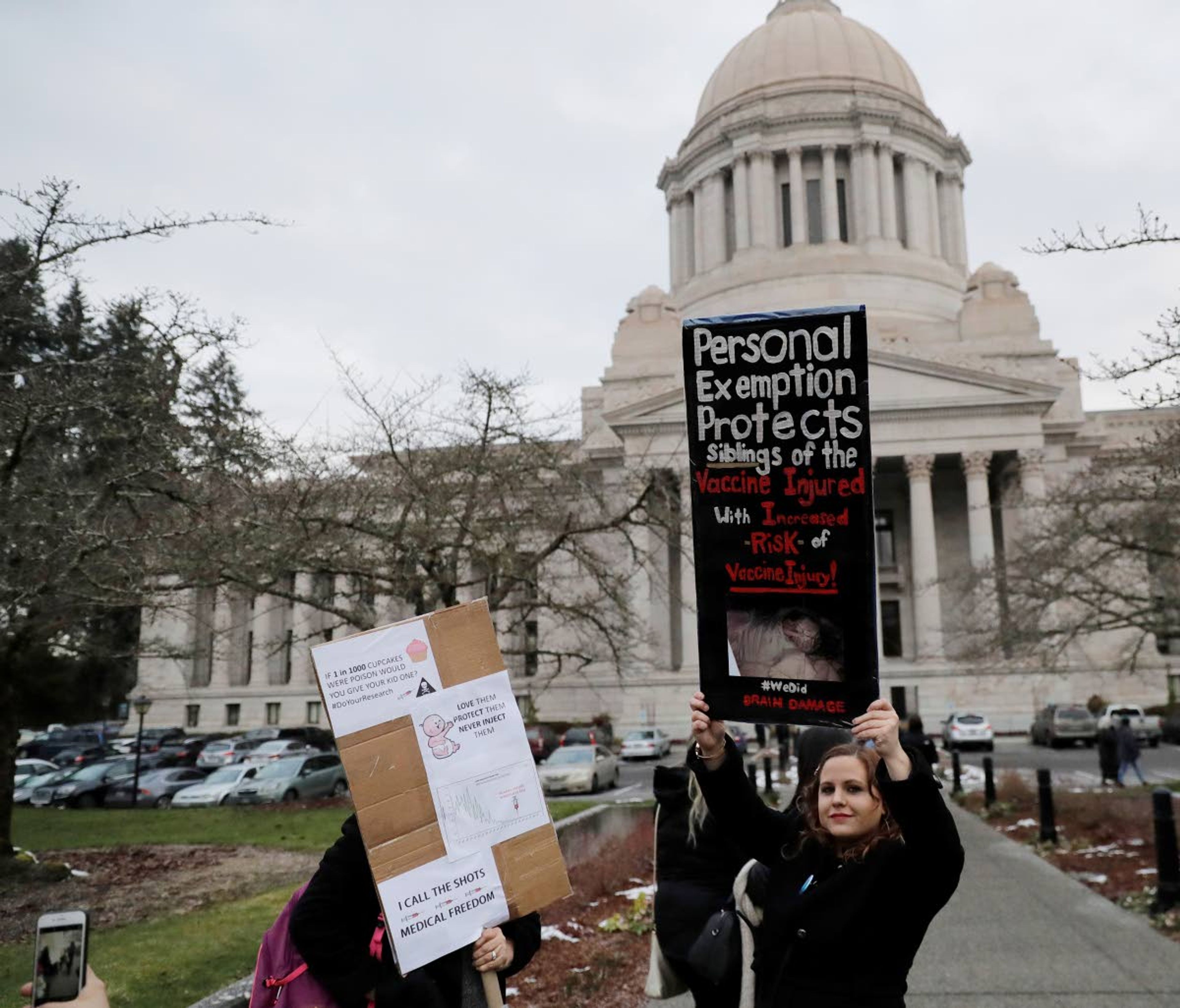 A woman holds a sign opposing a proposed bill that would remove parents’ ability to claim a philosophical exemption to opt their school-age children out of the combined measles, mumps and rubella vaccine as she stands Friday near the Legislative Building after a public hearing on the measure.