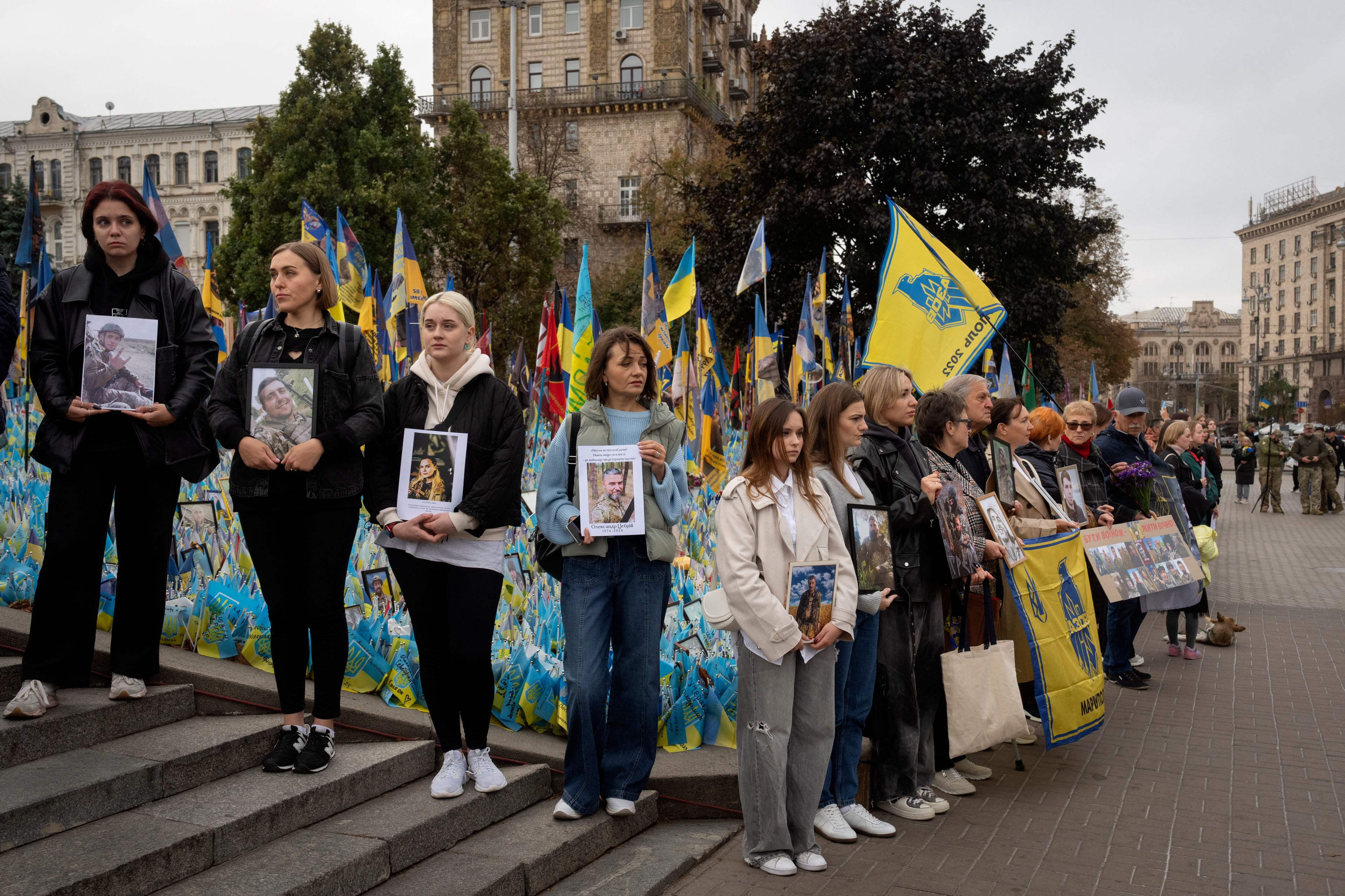 People hold photos of their relatives soldiers to keep a nationwide minute of silence in memory of fallen soldiers, who defended their homeland in war with Russia, on Defenders Day at the improvised war memorial in Independence square in Kyiv, Ukraine, Tuesday, Oct. 1, 2024. (AP Photo/Efrem Lukatsky)