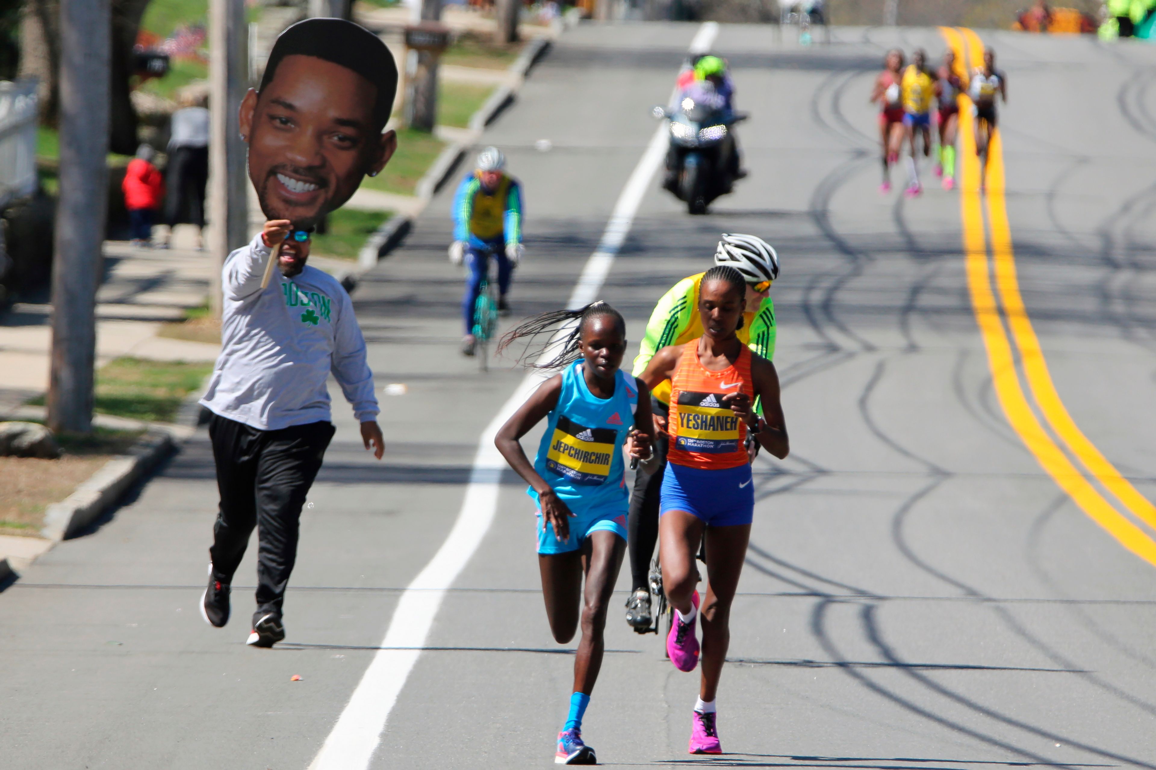 A man carrying a picture of actor Will Smith runs behind Peres Jepchirchir, of Kenya, left, and Ababel Yeshaneh, of Ethiopia, during the 126th Boston Marathon in Natick, Mass, Monday, April 18, 2022. (AP Photo/Jennifer McDermott)