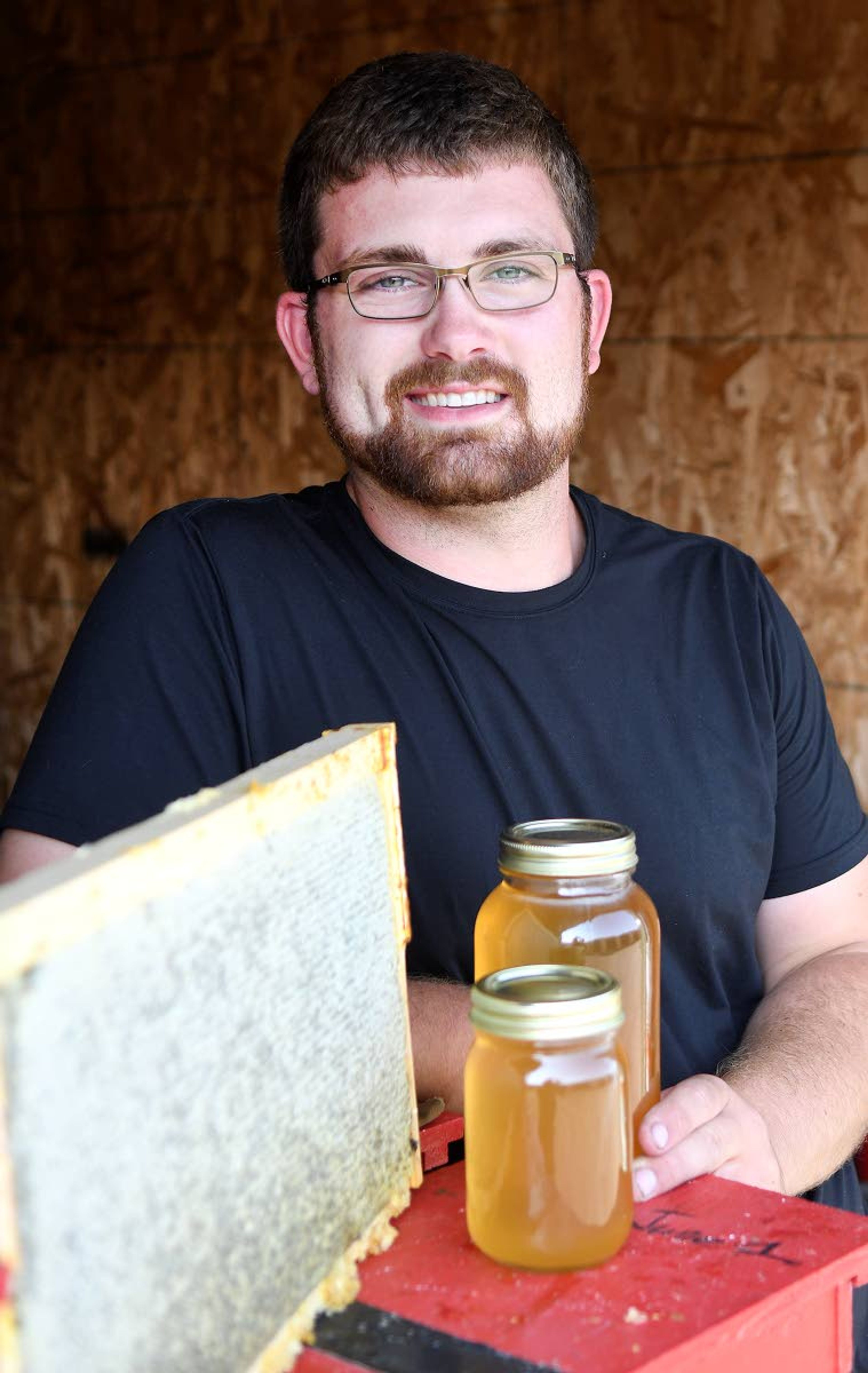 Professional beekeeper Jacob Waller of Clarkston display some jars of the honey his bees produce. Next to the jars is a beehive frame packed with honey-filled honeycomb and ready to be harvested.