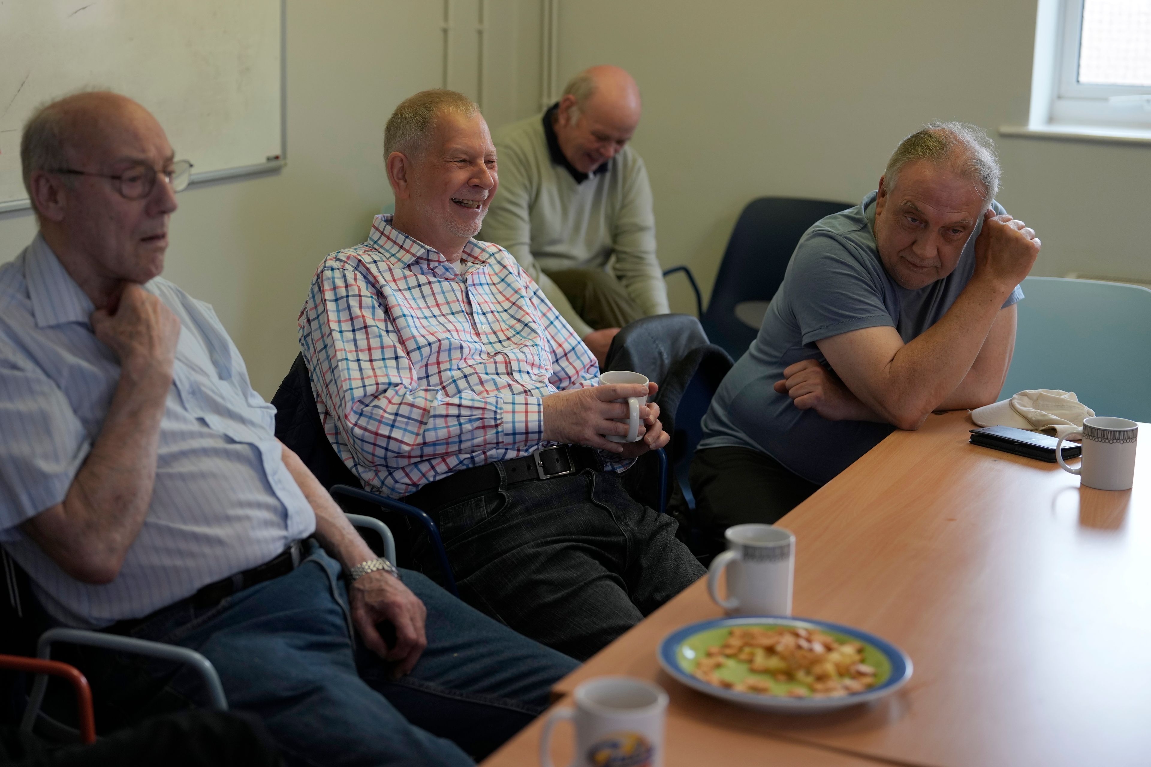 Alan Tucker, second left, listens at the weekly lunch meeting of some 20 retired men at the Tredegar community centre in Bow, in east London, Thursday, May 16, 2024. Passing around plates of cheese and crackers and slices of crème cake, they drank steaming coffee and tea. What they wanted was a chance to vent about the problems facing Britain and the fact that no one is listening to them as the country prepares for an election later this year. (AP Photo/Alastair Grant)