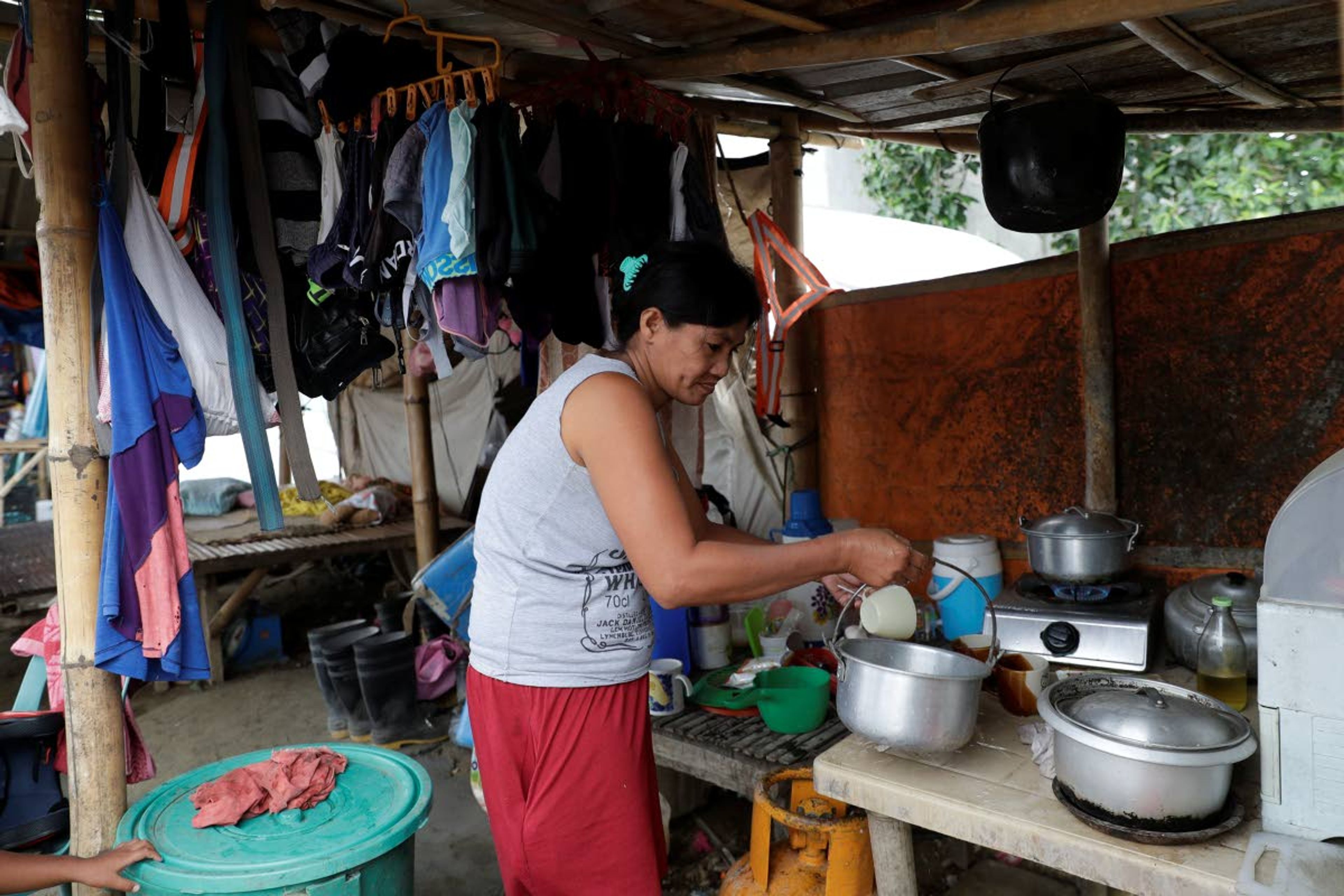 ABOVE: Luisa Silva, a former resident of Taal volcano, arranges her kitchen Jan. 10 in her family’s tent at a relocation site in Balete, Batangas province, Philippines.RIGHT: Fisherman Rogelito Cacao stands on a berm of mud and ash as he looks at the remains of his house at the Taal volcano.