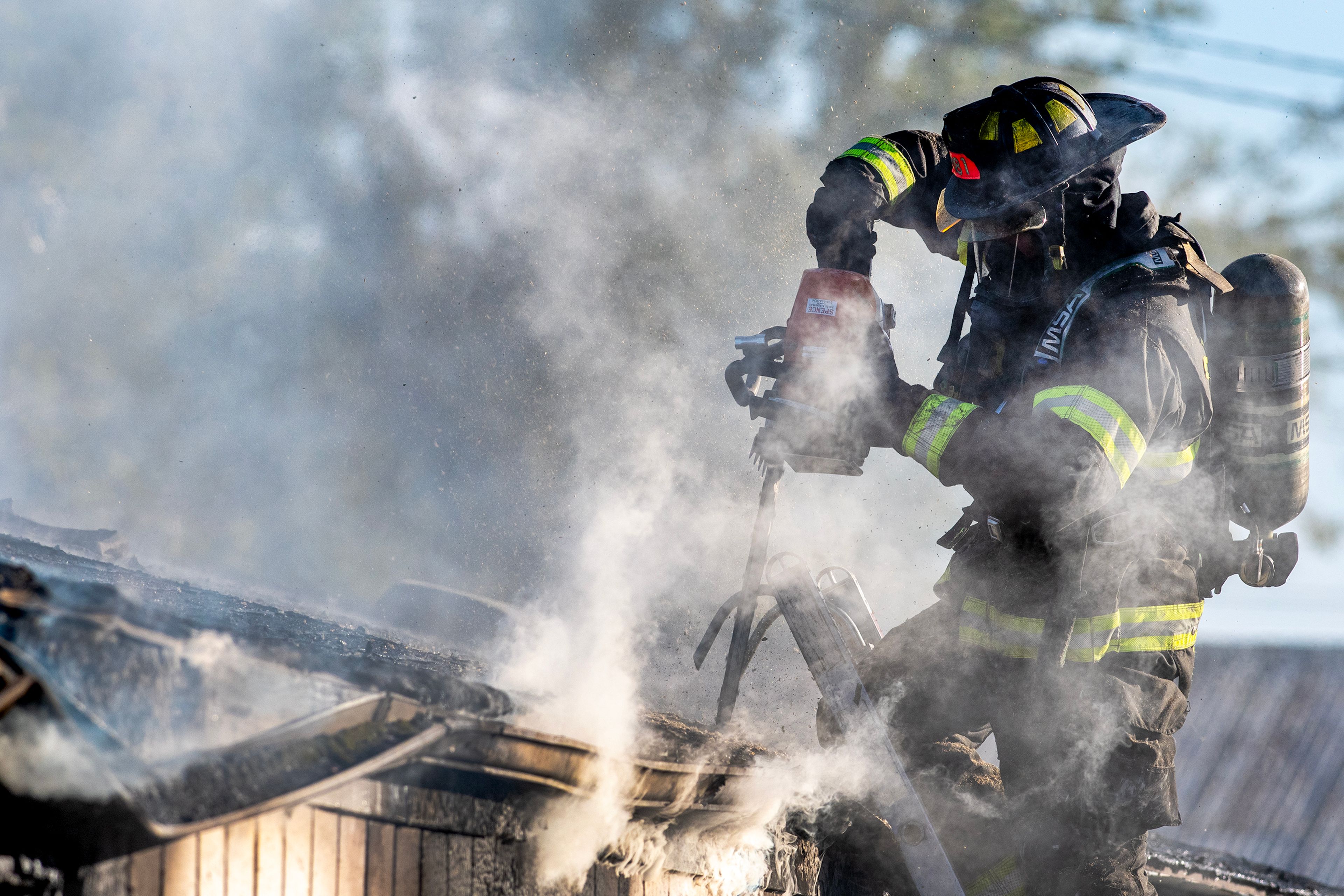 A firefighters uses a chainsaw to cut into the roof of a burning mobile home Thursday off 13th Street in Clarkston.