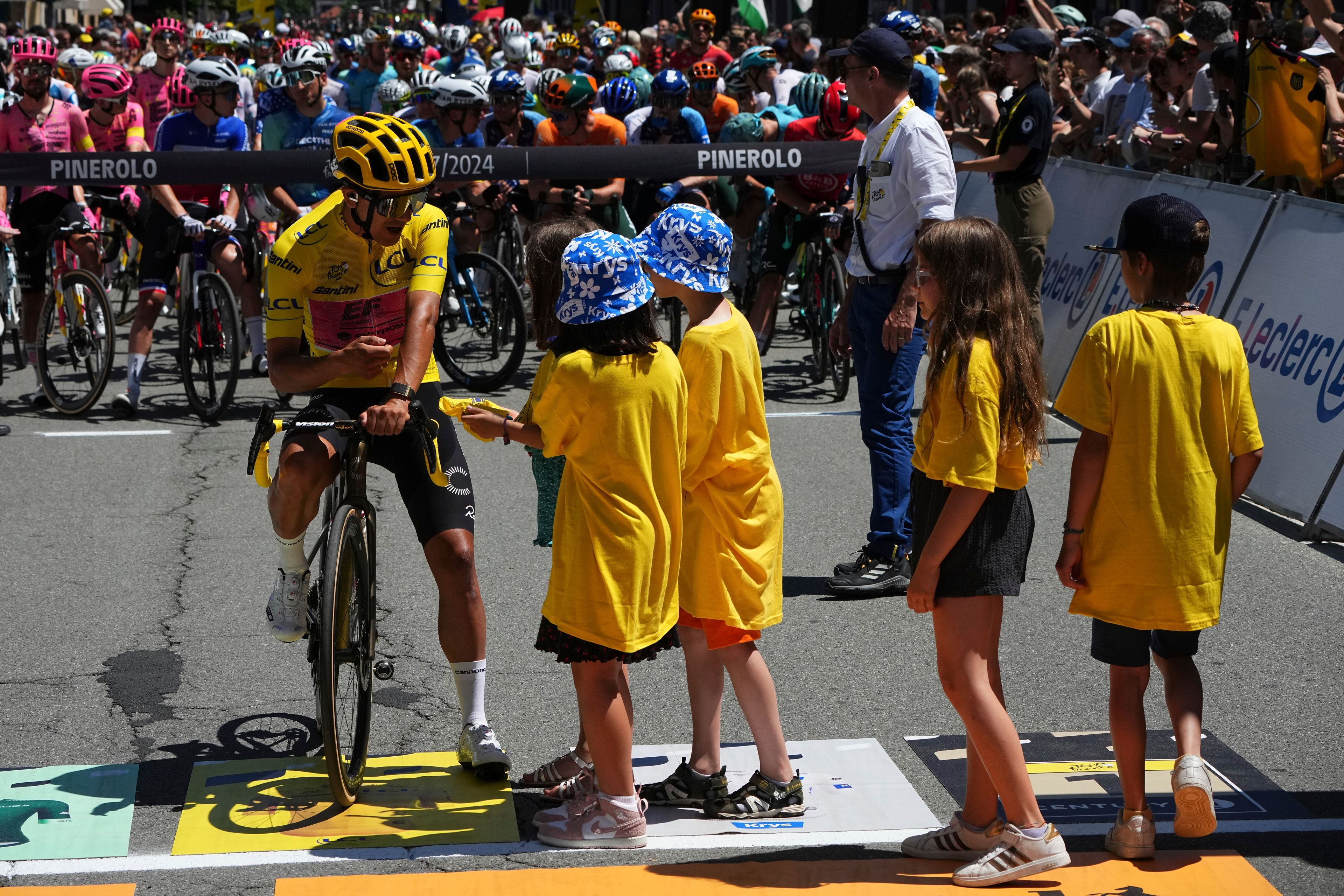 Ecuador's Richard Carapaz, wearing the overall leader's yellow jersey, talk with cycling fans as he waits for the start of the fourth stage of the Tour de France cycling race over 139.6 kilometers (86.7 miles) with start in Pinerolo, Italy and finish in Valloire, France, Tuesday, July 2, 2024. (AP Photo/Daniel Cole)