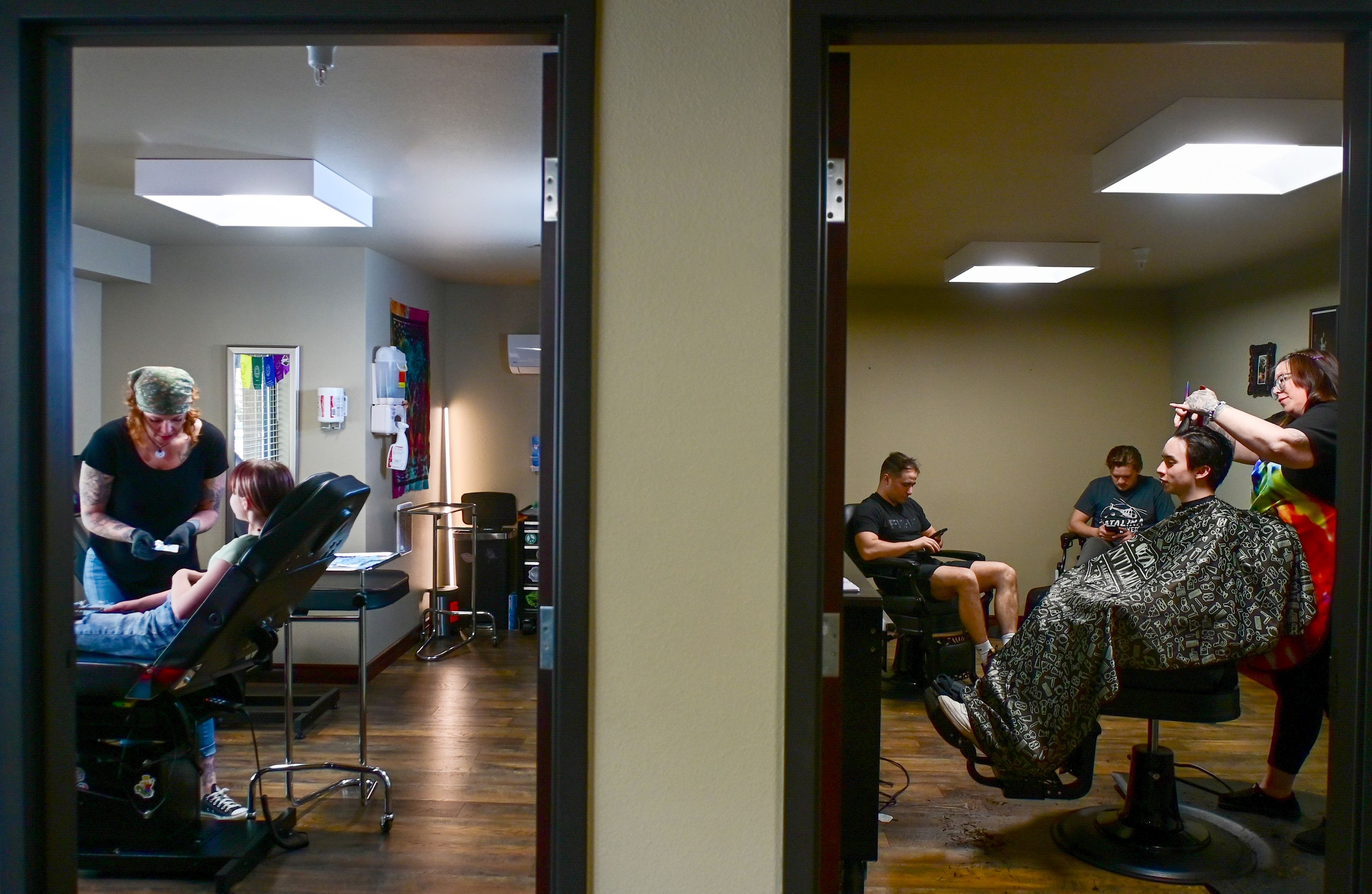 Blood Diamond Ink co-owner Sara Peltier, left, talks through piercings with Lillian Szumlas, 13, of Pullman, while Washington State University student Nate Trahan sits in the barber chair to discuss a haircut with Diamond’s Edge Barbershop ownerBroooke Moore next door in the new expanded space of the tattoo shop, Wednesday, April 17, in Pullman.