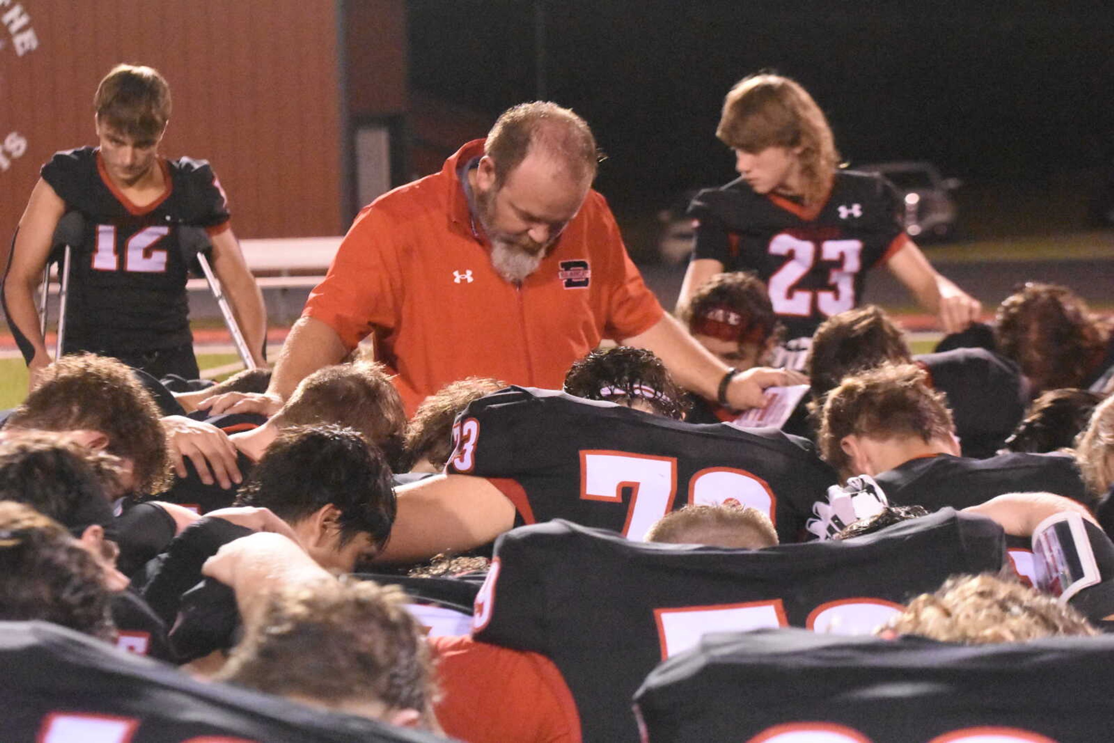 The Dexter football team takes a knee with head coach Chad Jamerson for a post game prayer.