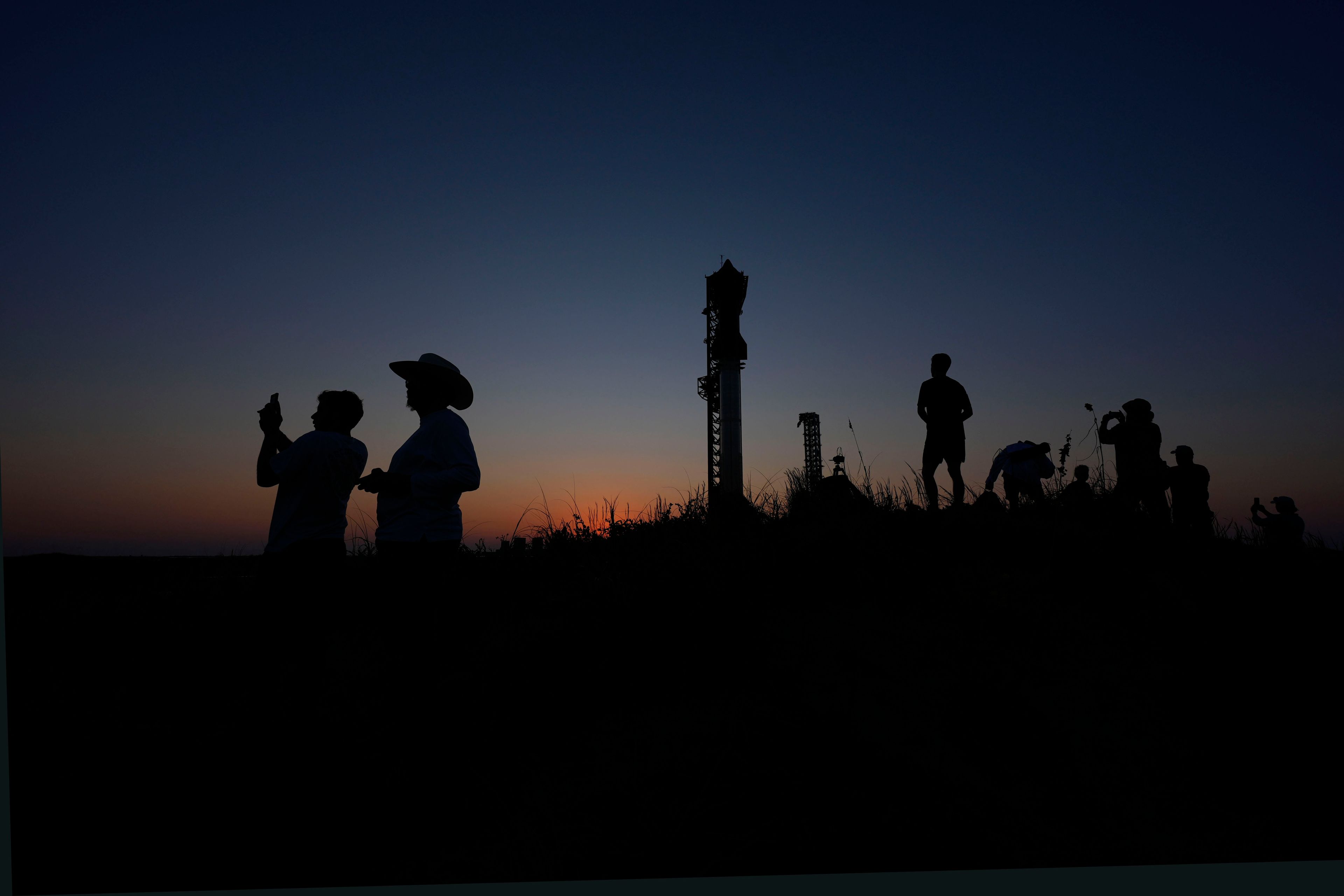 People take photos as the sun sets behind SpaceX's mega rocket Starship, Saturday, Oct. 12, 2024, in Boca Chica, Texas. (AP Photo/Eric Gay)